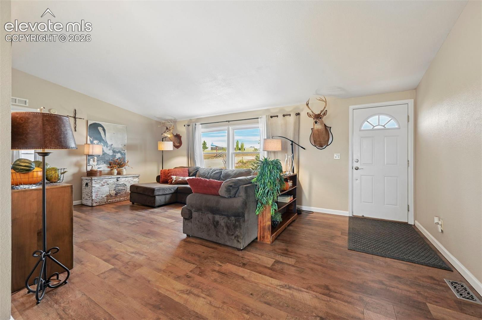 Living space featuring wood-finish flooring, vaulted ceilings, and a white front entry door with an arched glass panel