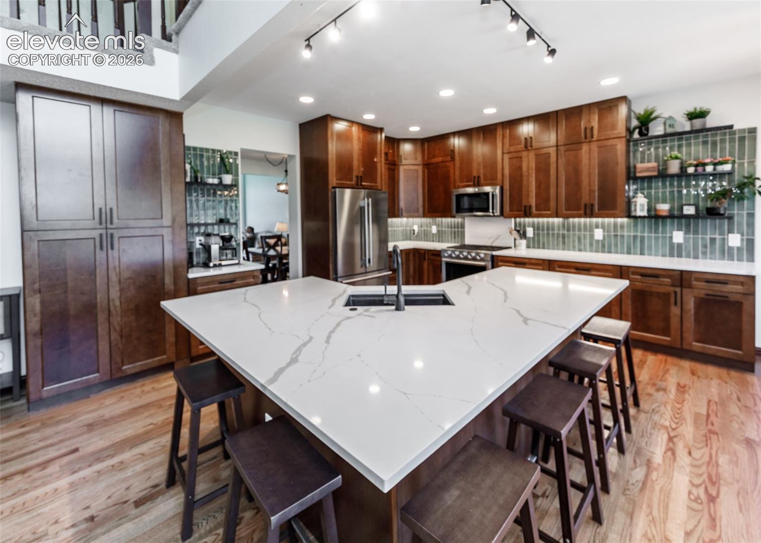 Kitchen featuring a large island with white stone-finish countertop, wood-finish flooring, full-height cabinetry, and stainless steel appliances