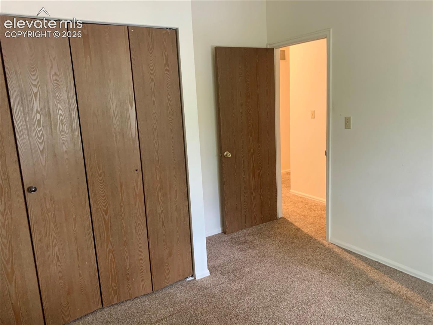 Wood-finish bifold closet doors, light neutral wall color, and textured carpeting