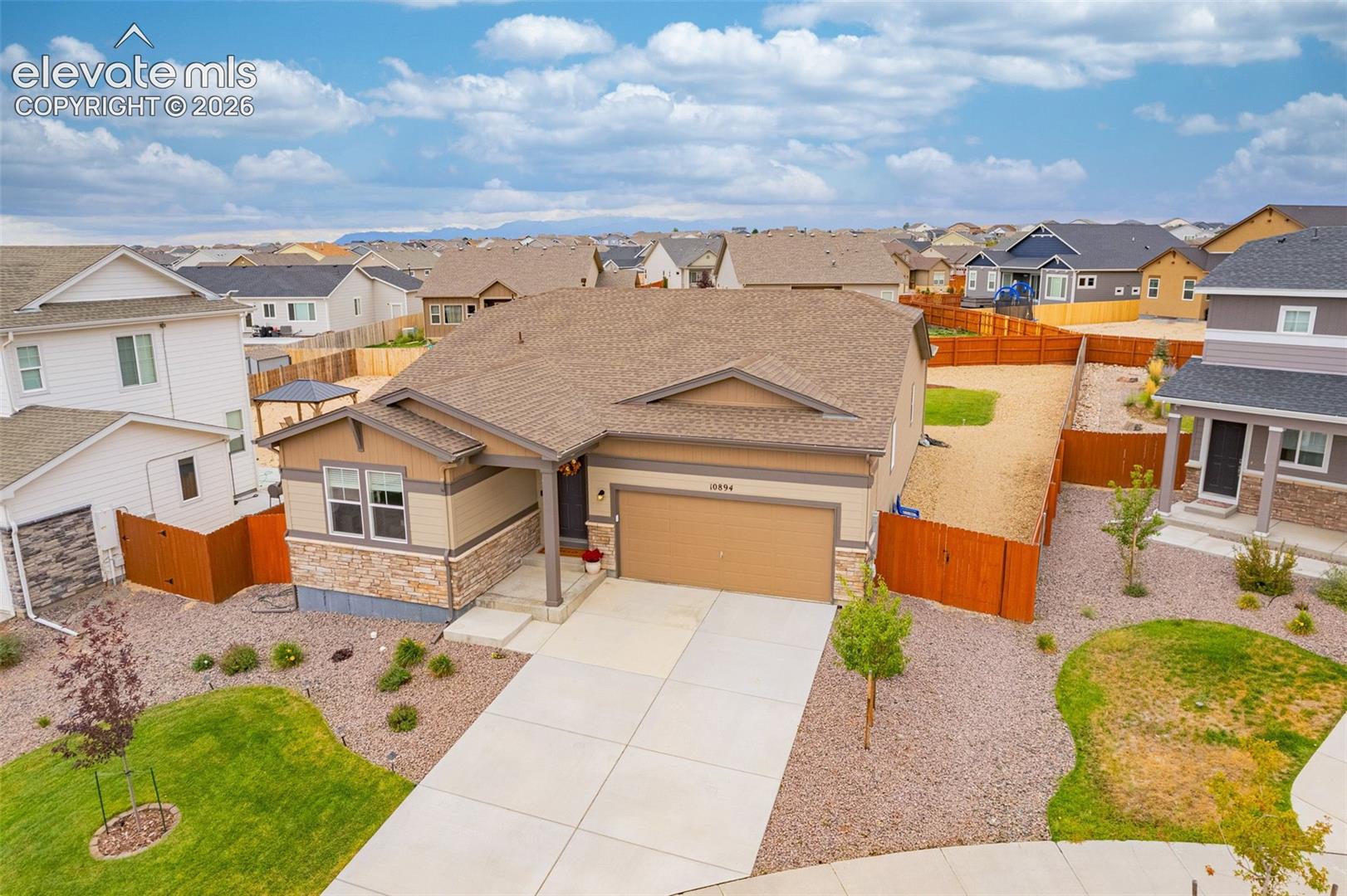 Multi-tone exterior with stone accents, attached two-car garage, concrete driveway, fenced yard, and landscaped front yard