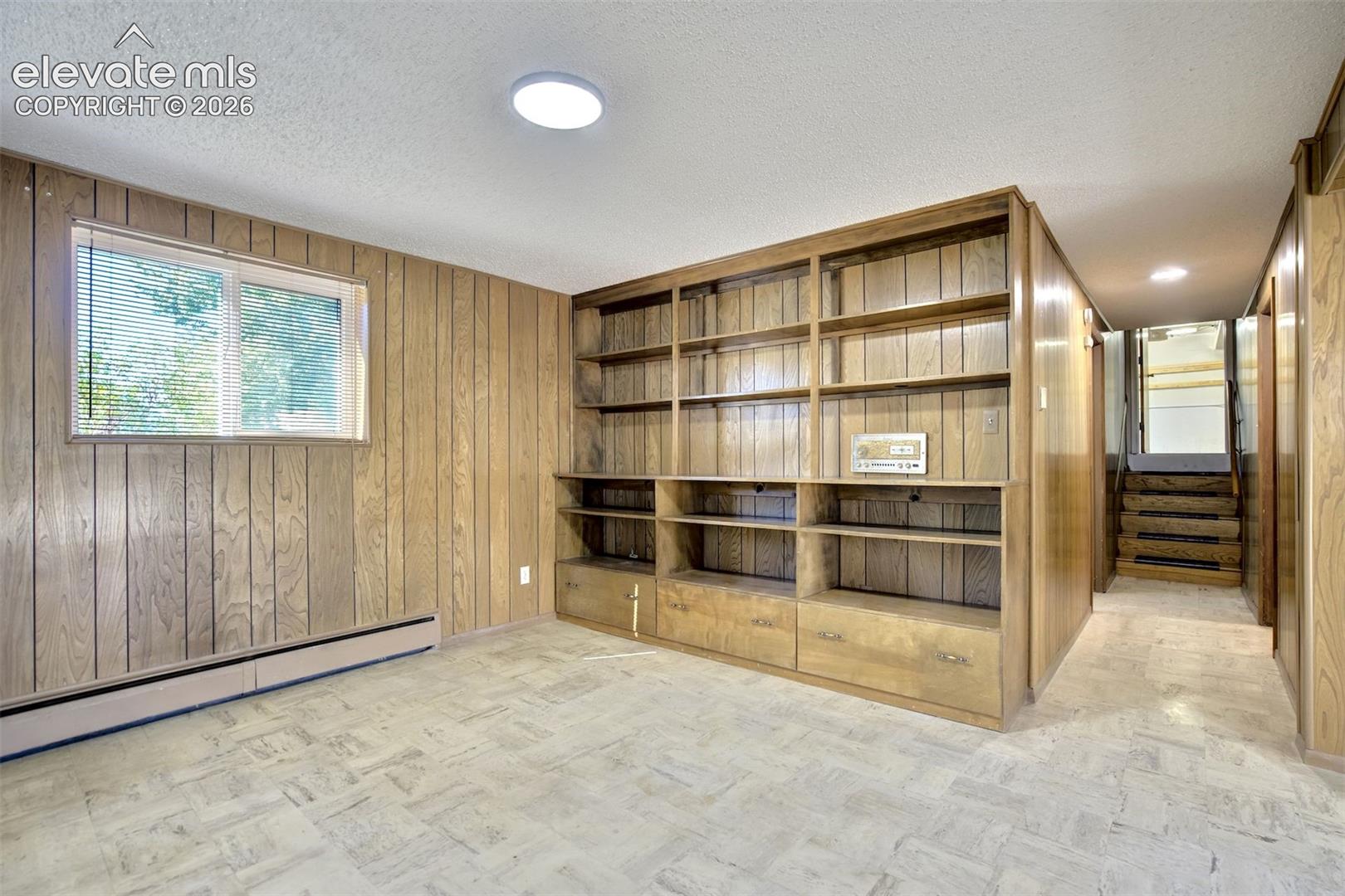Interior space featuring wood paneling, floor-to-ceiling built-in wooden cabinetry with shelving and storage drawers, stone-finish tile flooring, and a window with horizontal blinds