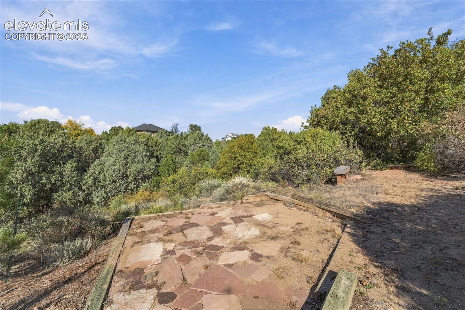 Flagstone patio with timber edging, expansive natural terrain, and mature native trees