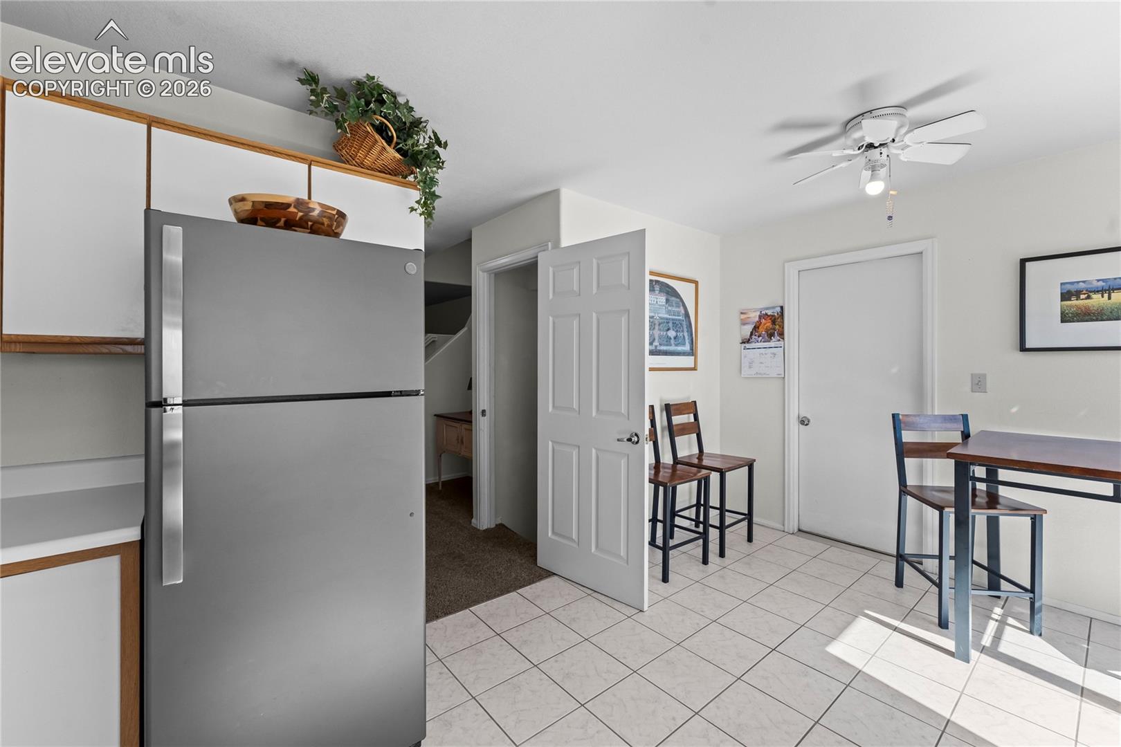 White tile flooring, ceiling fan, white paneled doors, built-in cabinetry, and a stainless steel refrigerator