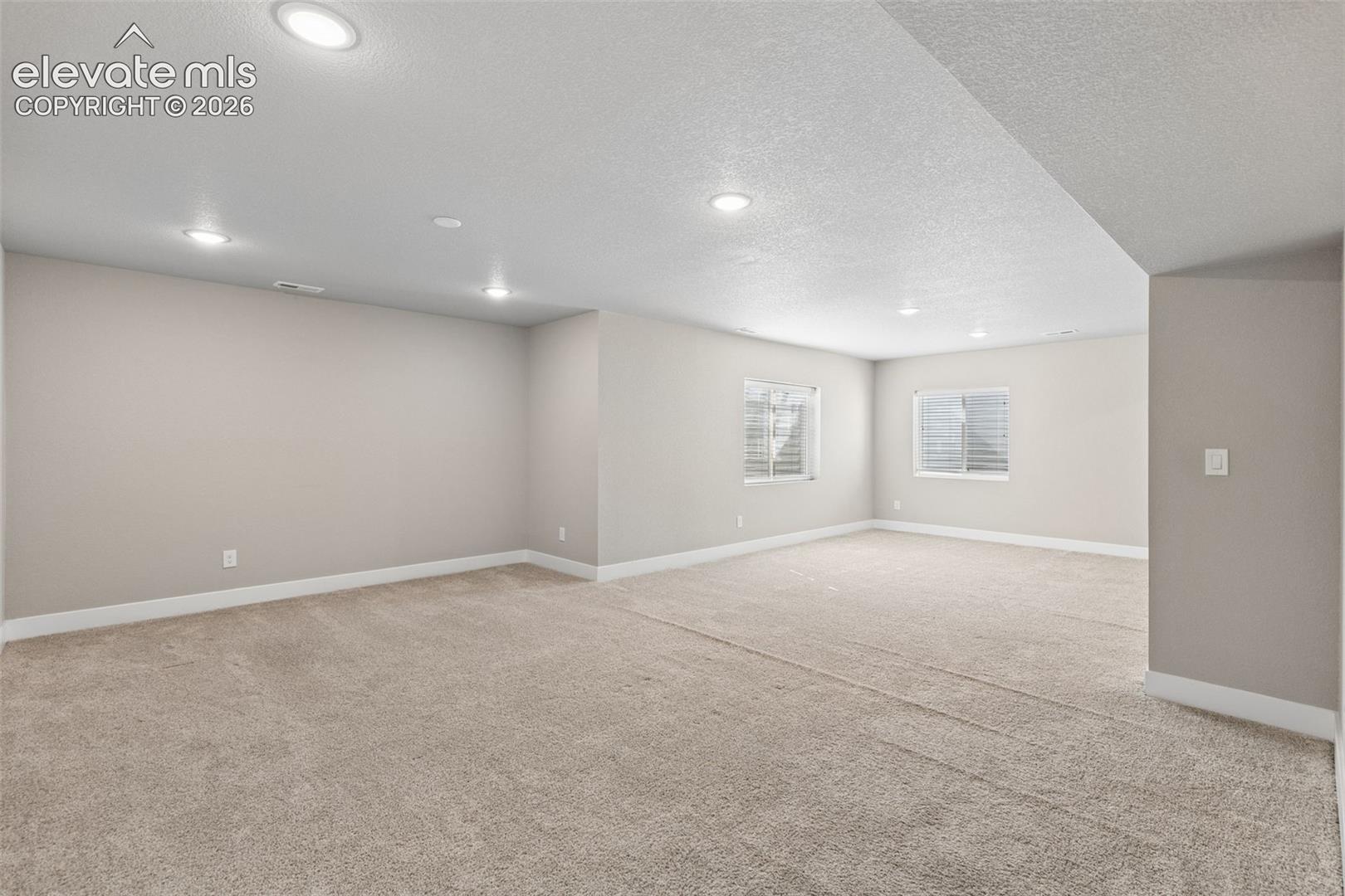 Neutral interior featuring wall-to-wall carpeting, recessed ceiling lighting, and egress windows with window wells