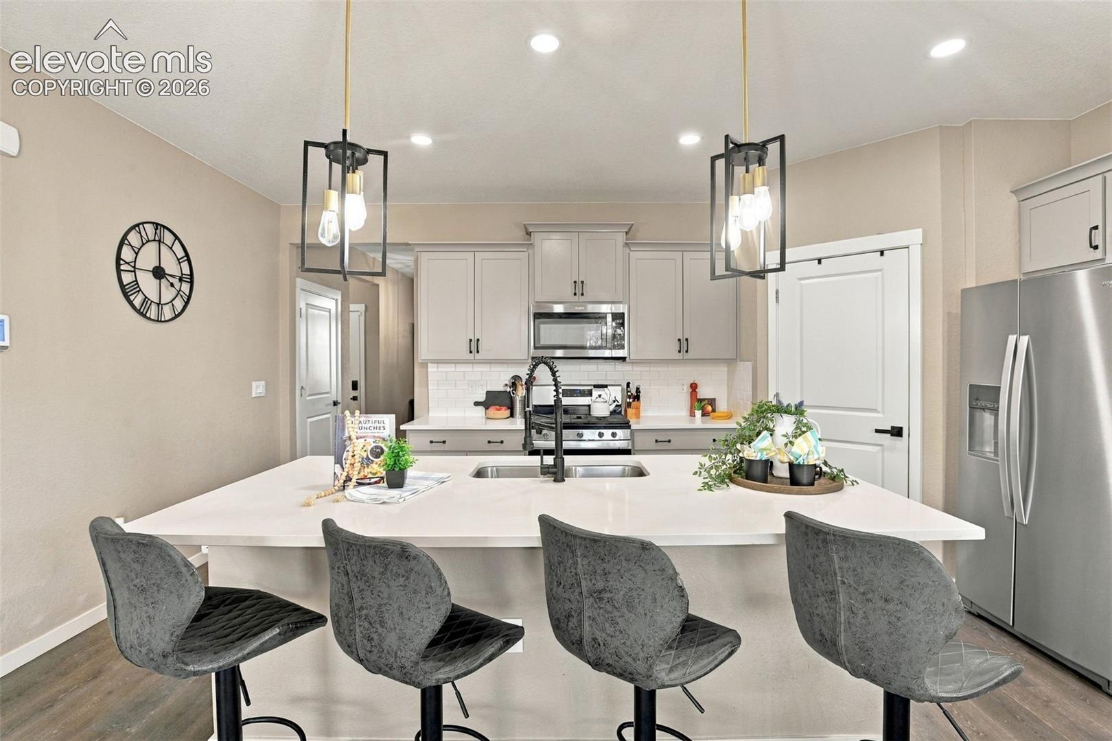 Kitchen featuring a central island with a solid surface countertop, Shaker-style cabinetry, stainless steel appliances, matte black hardware, and dual geometric pendant lights