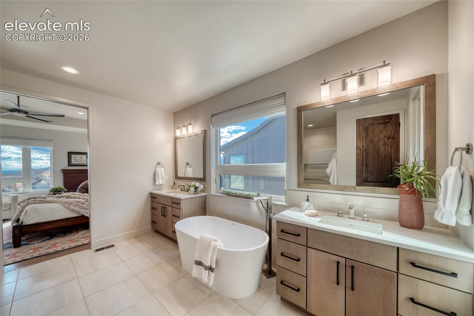 Bathroom featuring a freestanding oval soaking tub, double vanity with light wood-finish cabinetry, rectangular vessel sinks, framed mirrors, and recessed lighting