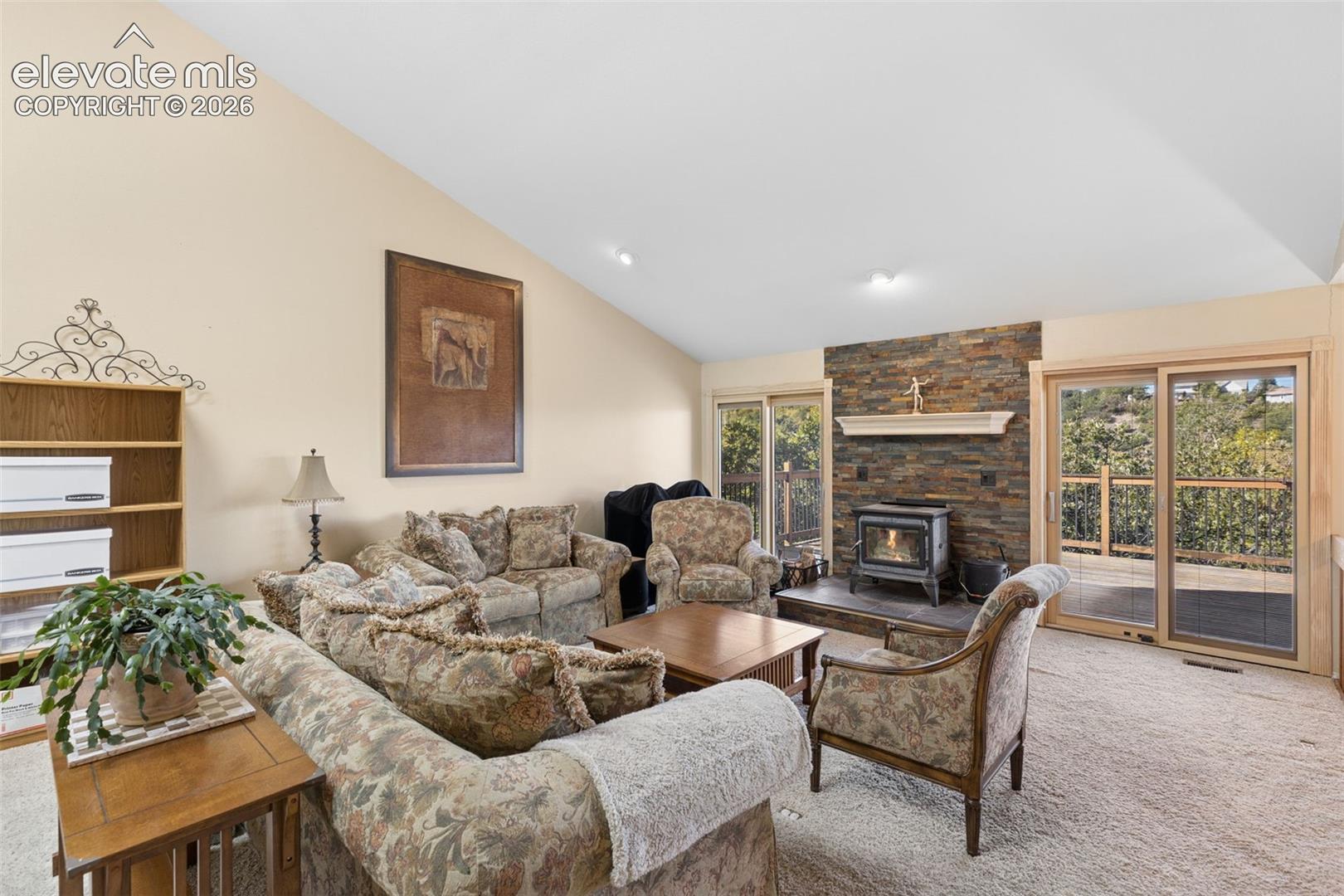 Vaulted ceiling, stone-surround fireplace with a wood-burning stove, built-in wooden shelving, and dual sliding glass doors