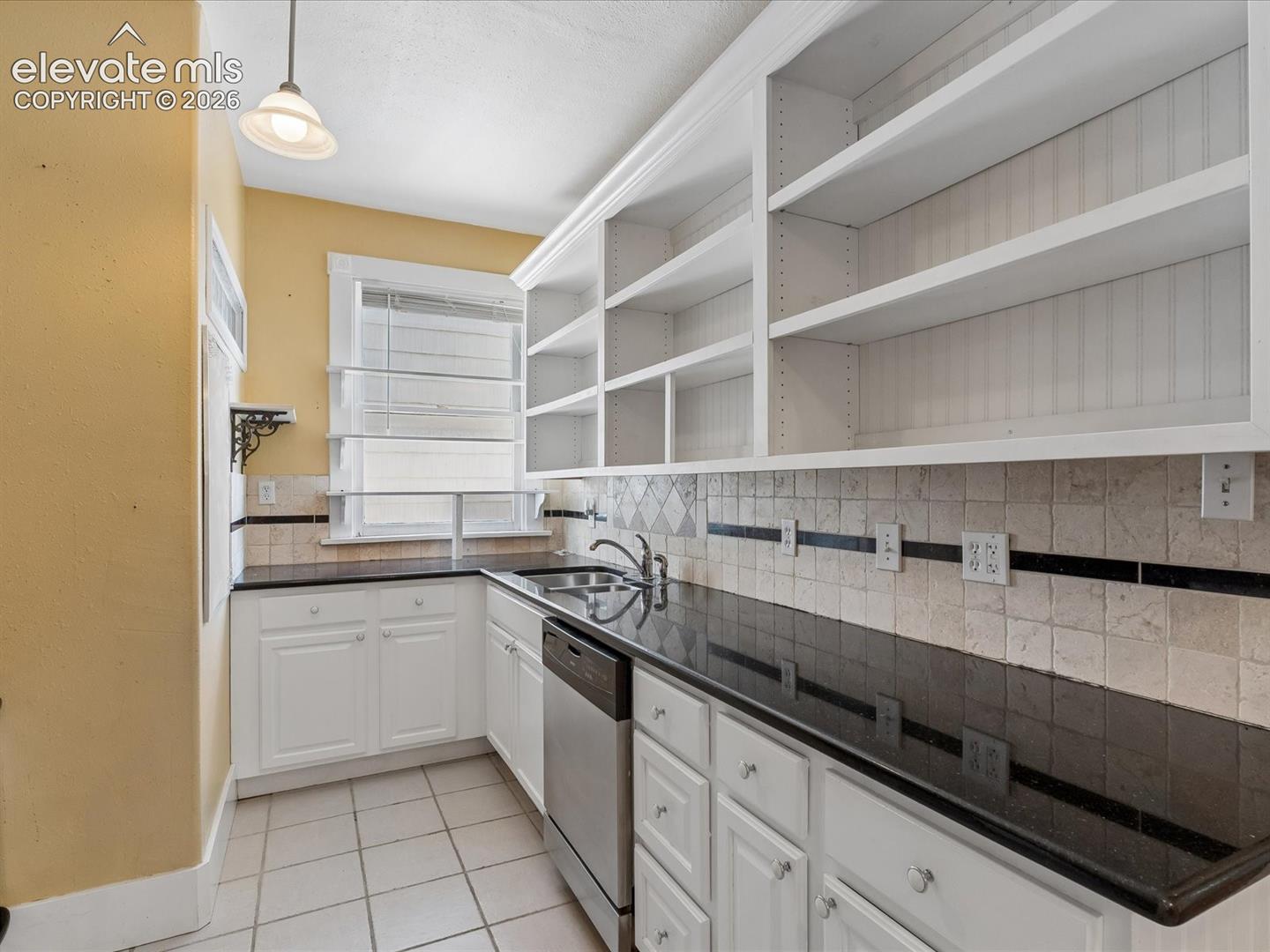 Kitchen featuring open shelving, white cabinetry, dark countertops, a stainless steel dishwasher, and a tile backsplash