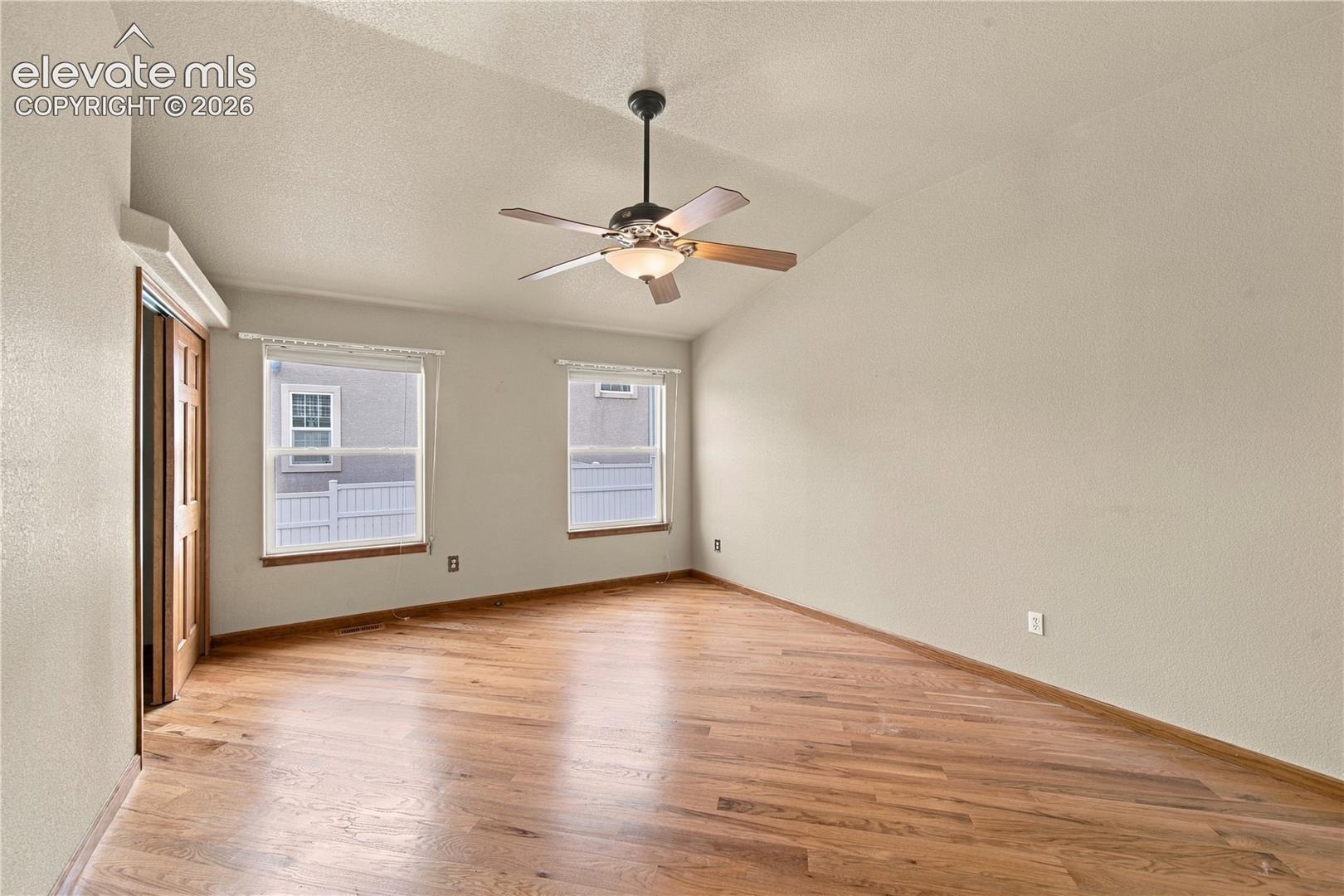 Vaulted ceiling featuring a central lighted ceiling fan, wood-finish flooring, and dual windows