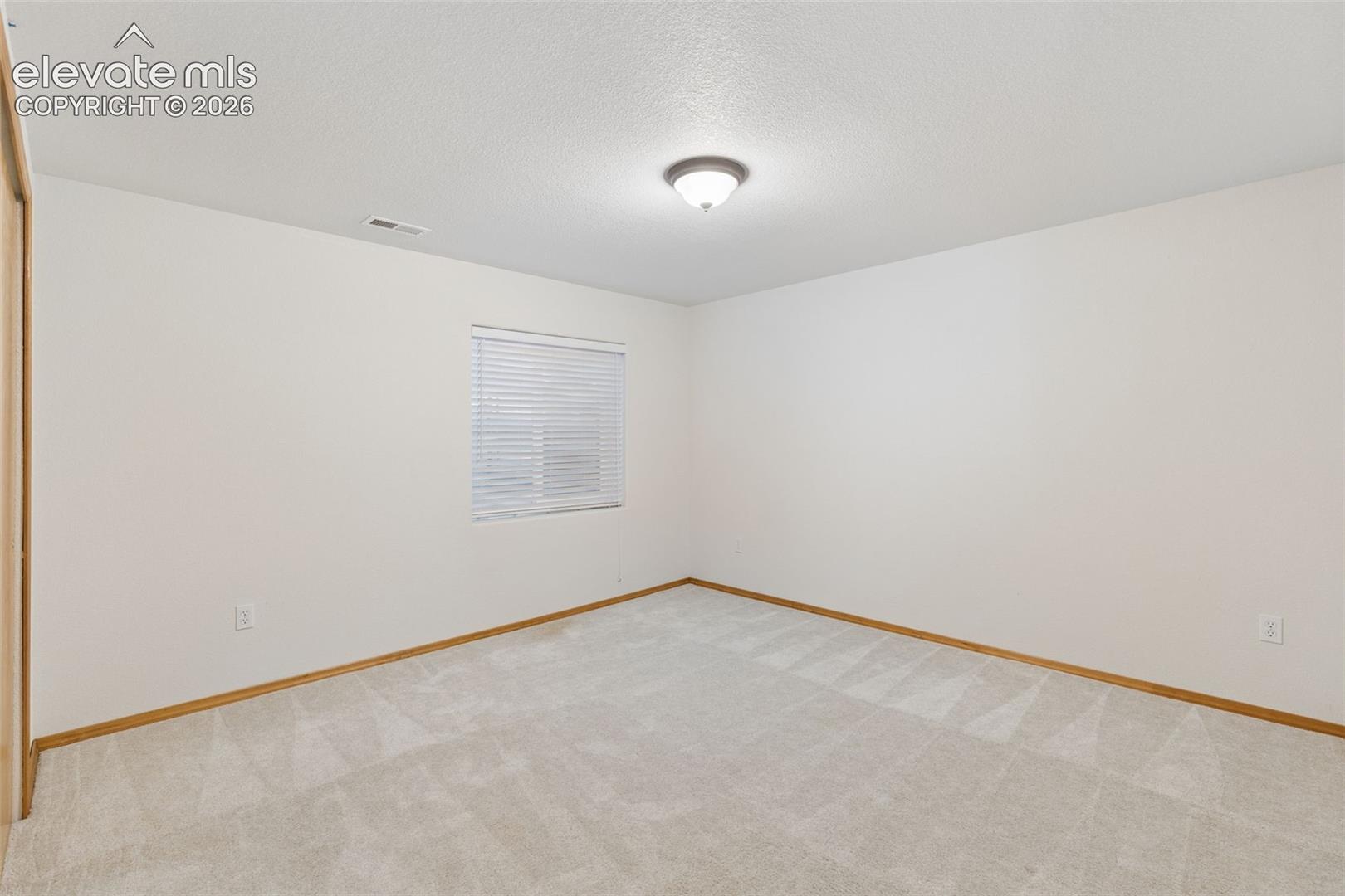 Neutral-toned wall-to-wall carpeting, window with horizontal blinds, flush-mount ceiling lighting, and sliding-door closet