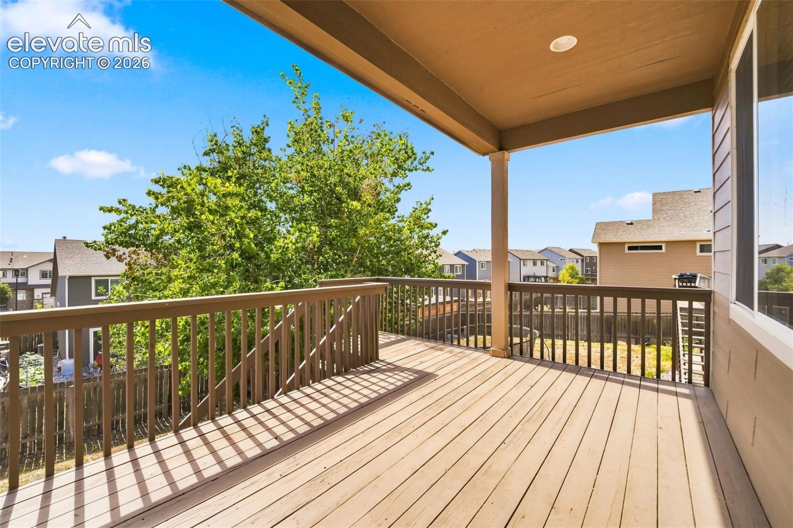 Expansive wood deck with a full railing system, covered patio area, and recessed ceiling lighting