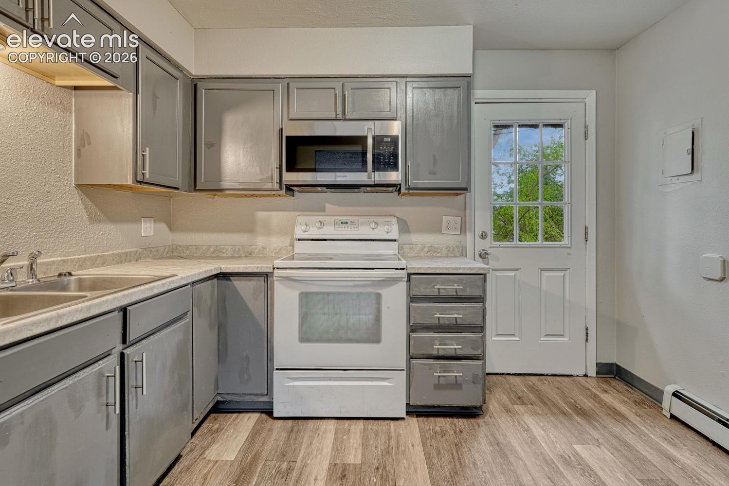 Kitchen featuring wood-finish flooring, gray cabinetry, a double basin sink, and a white electric range