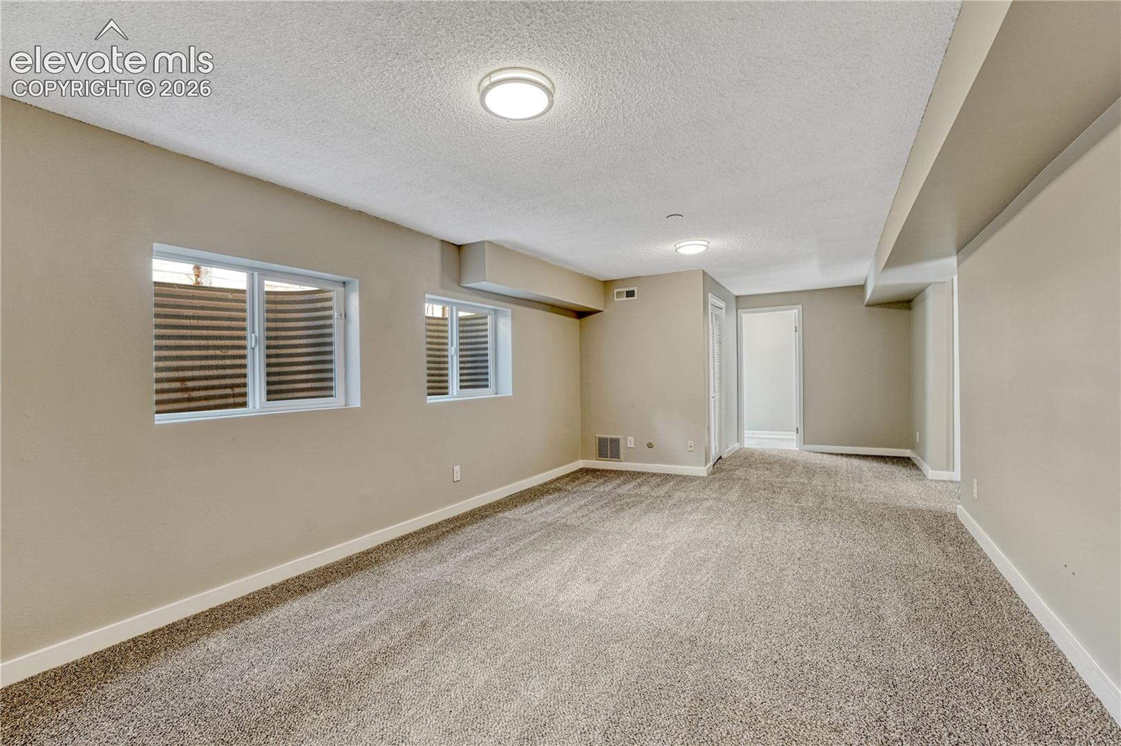 Spacious room featuring neutral wall finishes, recessed ceiling lighting, multiple windows with plantation shutters providing natural light, and neutral carpet flooring throughout