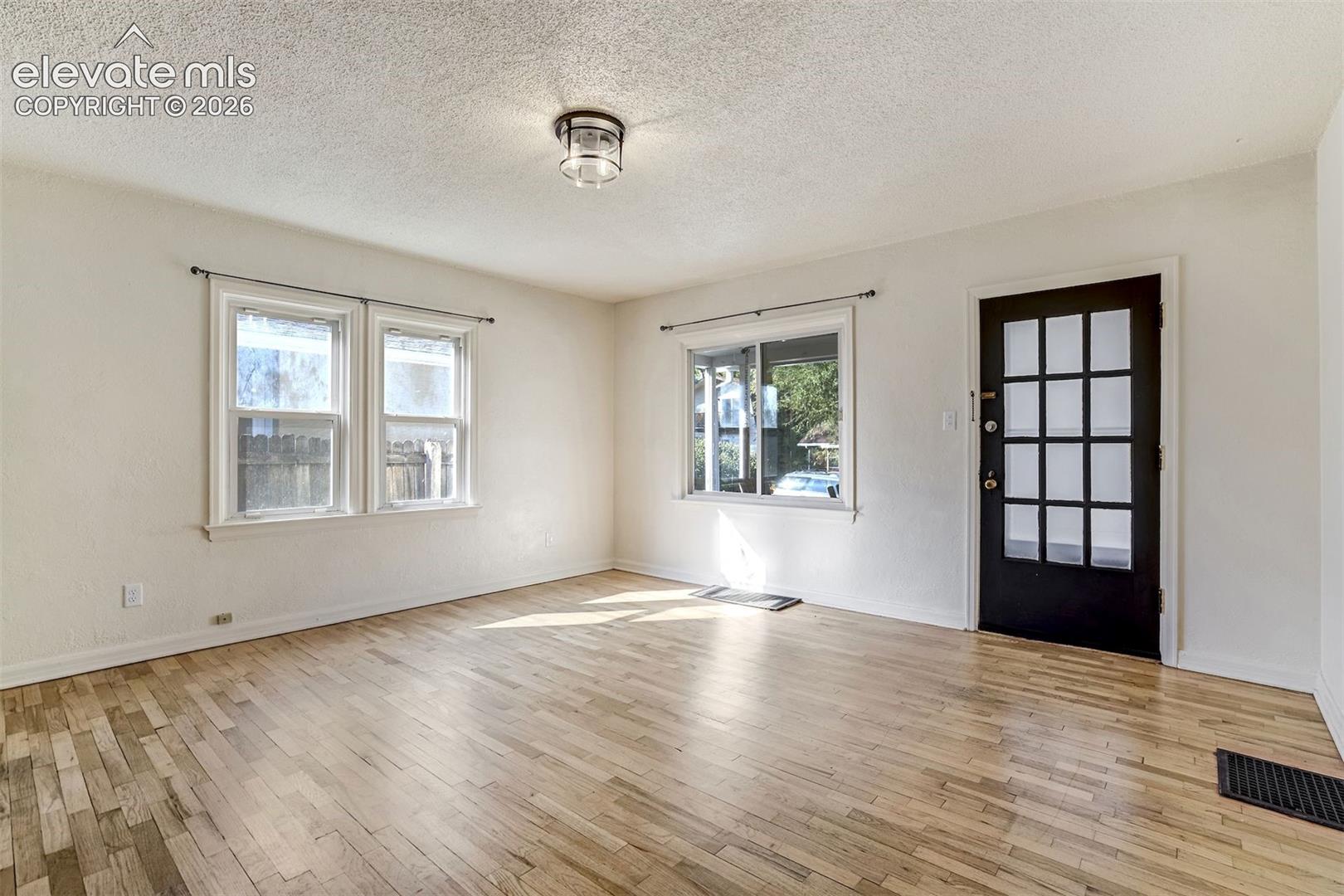 Interior space featuring wood-finish flooring, white walls, multiple windows, and a dark-toned exterior door with a multi-pane glass insert