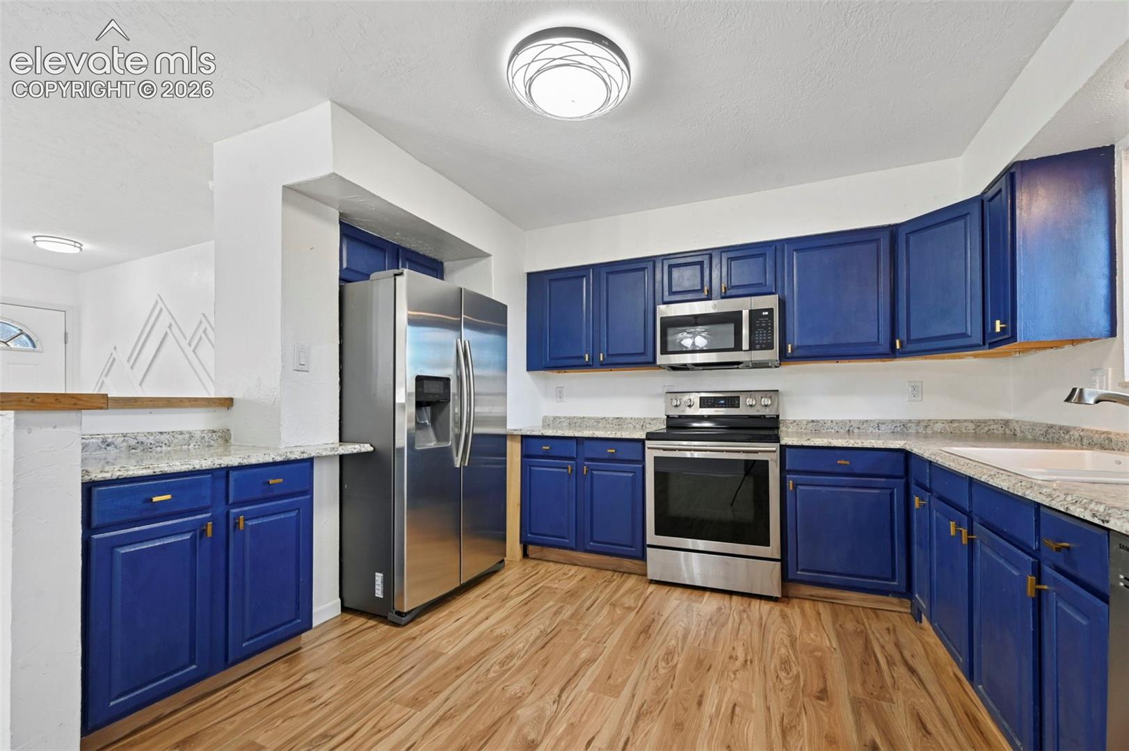 Kitchen featuring blue cabinetry, light-toned stone-patterned (formica) countertops, new LVP flooring, and stainless steel appliances including a side-by-side refrigerator, over-the-range microwave, and electric range