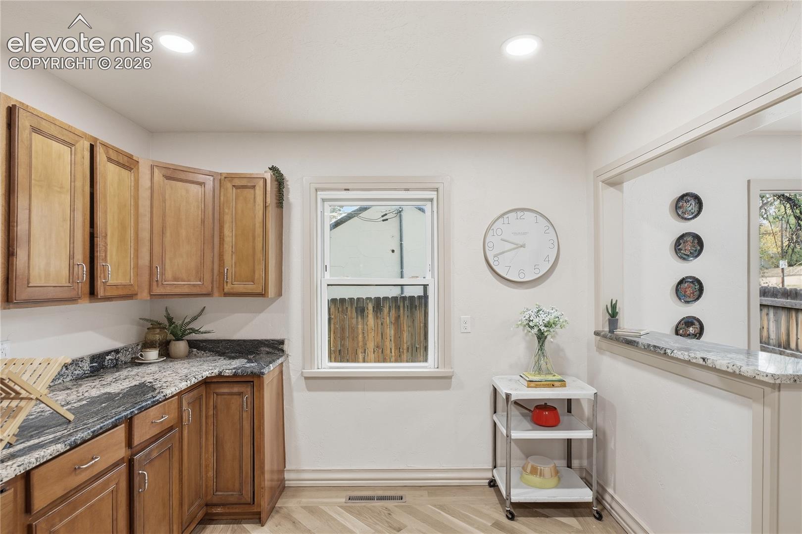 Kitchen featuring wood cabinetry, stone countertops, herringbone-patterned flooring, and a pass-through opening