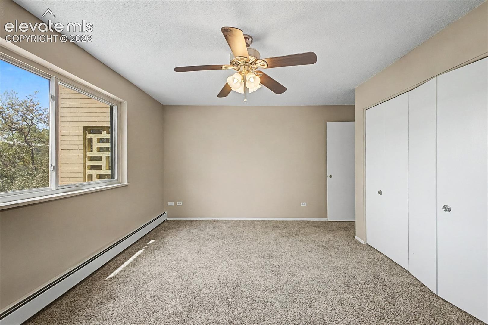 Carpeted room with a multi-pane window, flush-mounted ceiling fan, and built-in bi-fold closet doors