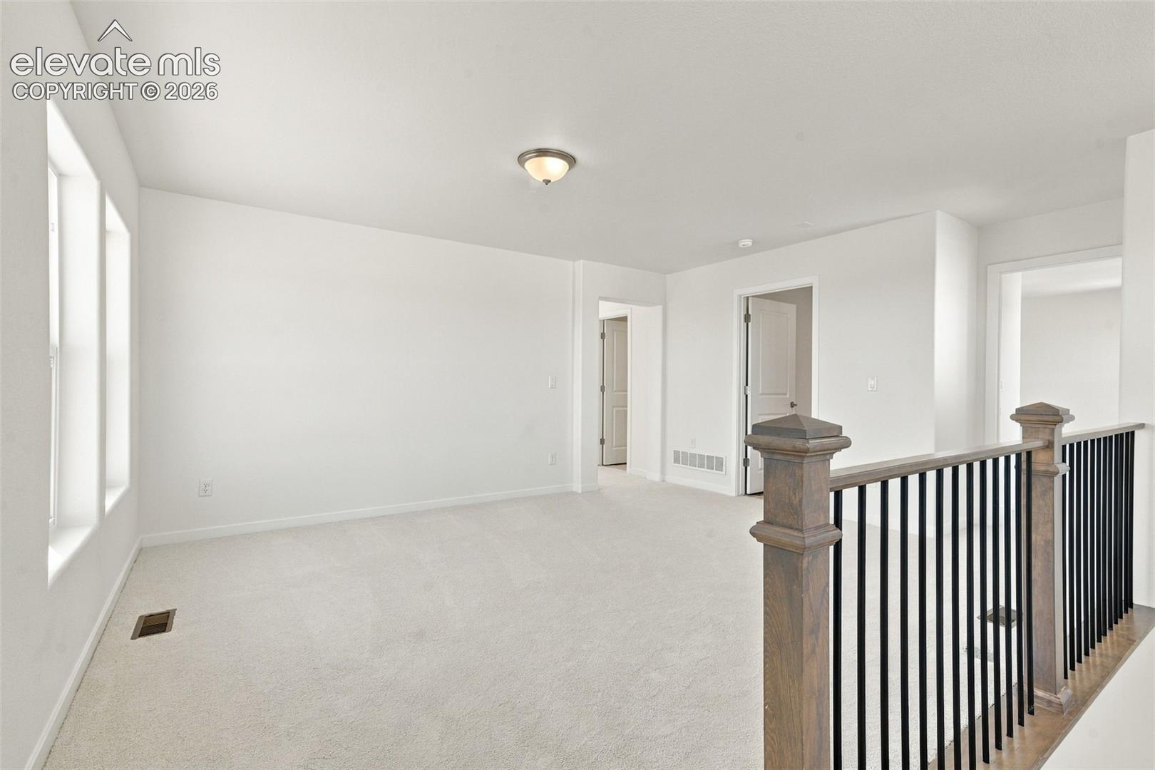 Carpeted room featuring multiple windows, a ceiling-mounted light fixture, and a railing with wood-finish newel posts and black balusters