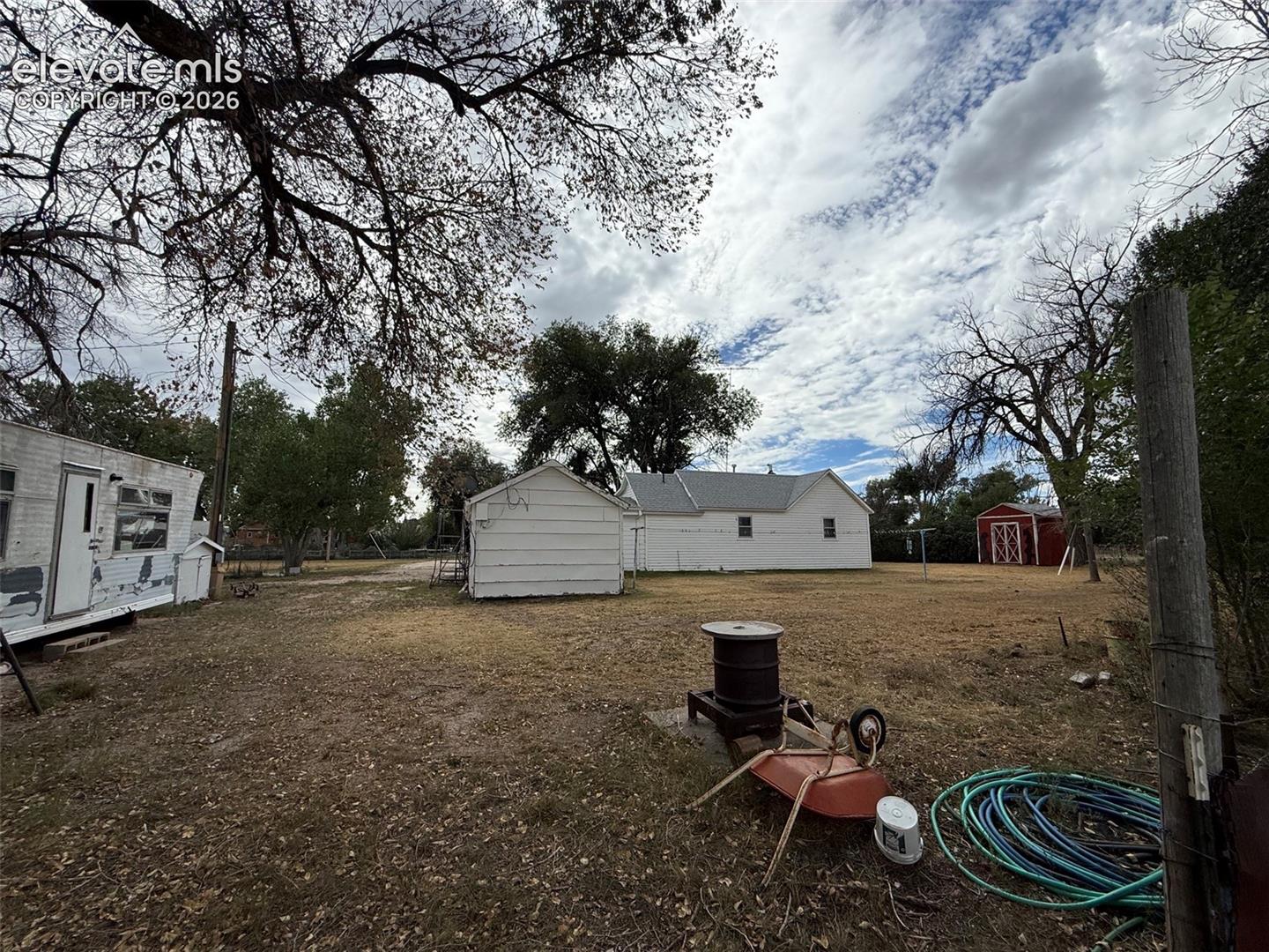 Expansive open lot featuring multiple detached structures, mature trees, and a red exterior storage shed