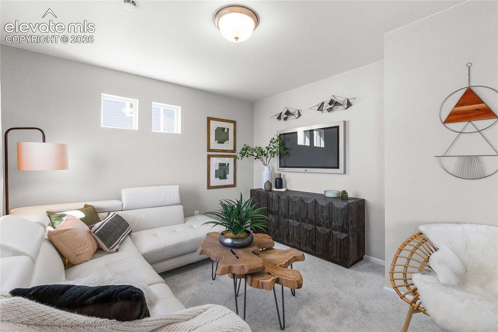 Modern living room featuring a light gray carpeted floor, sectional seating with neutral upholstery, and a wood-finish coffee table with metal hairpin legs
*photos of a model home*