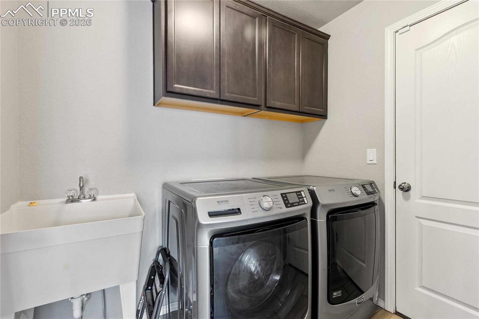 Convenient laundry room with upper cabinetry and utility sink