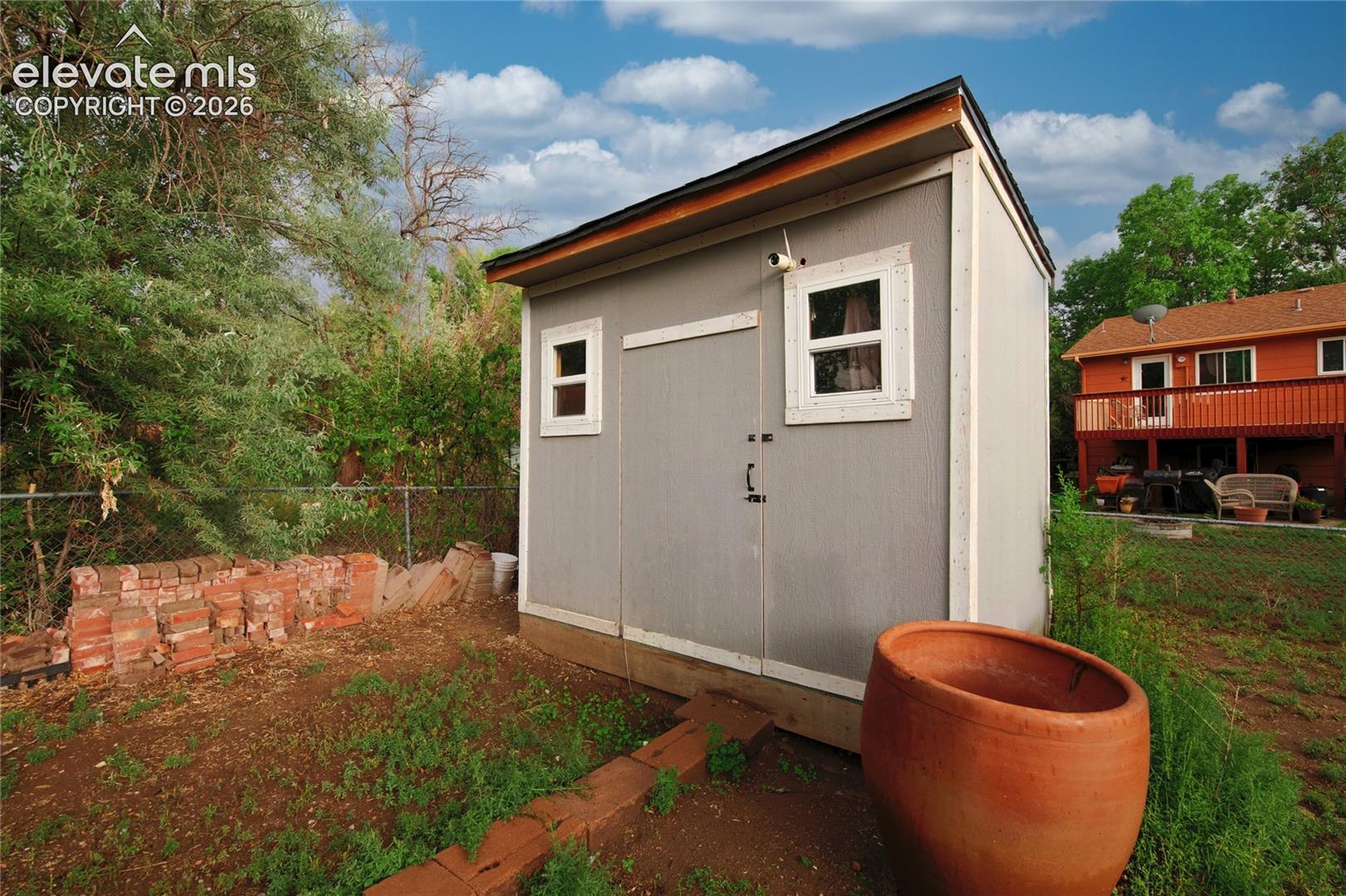Modern storage shed featuring a gable roof with contrasting trim, horizontal siding in soft gray, dual windows with white frames, and a wide hinged door