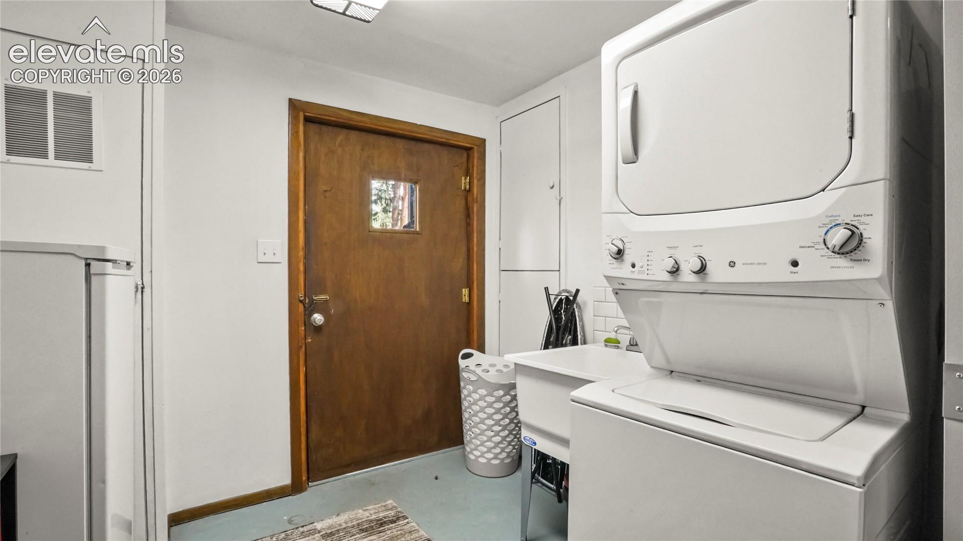 Stackable washer and dryer, utility sink, and white subway tile backsplash, walk out from basement.