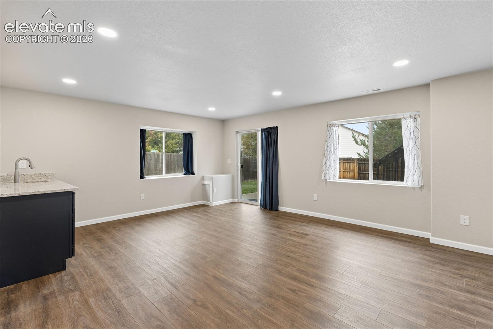 Open-concept interior featuring wood-finish flooring, recessed lighting, double-pane windows, and a built-in wet bar with a stone-finish countertop and sink