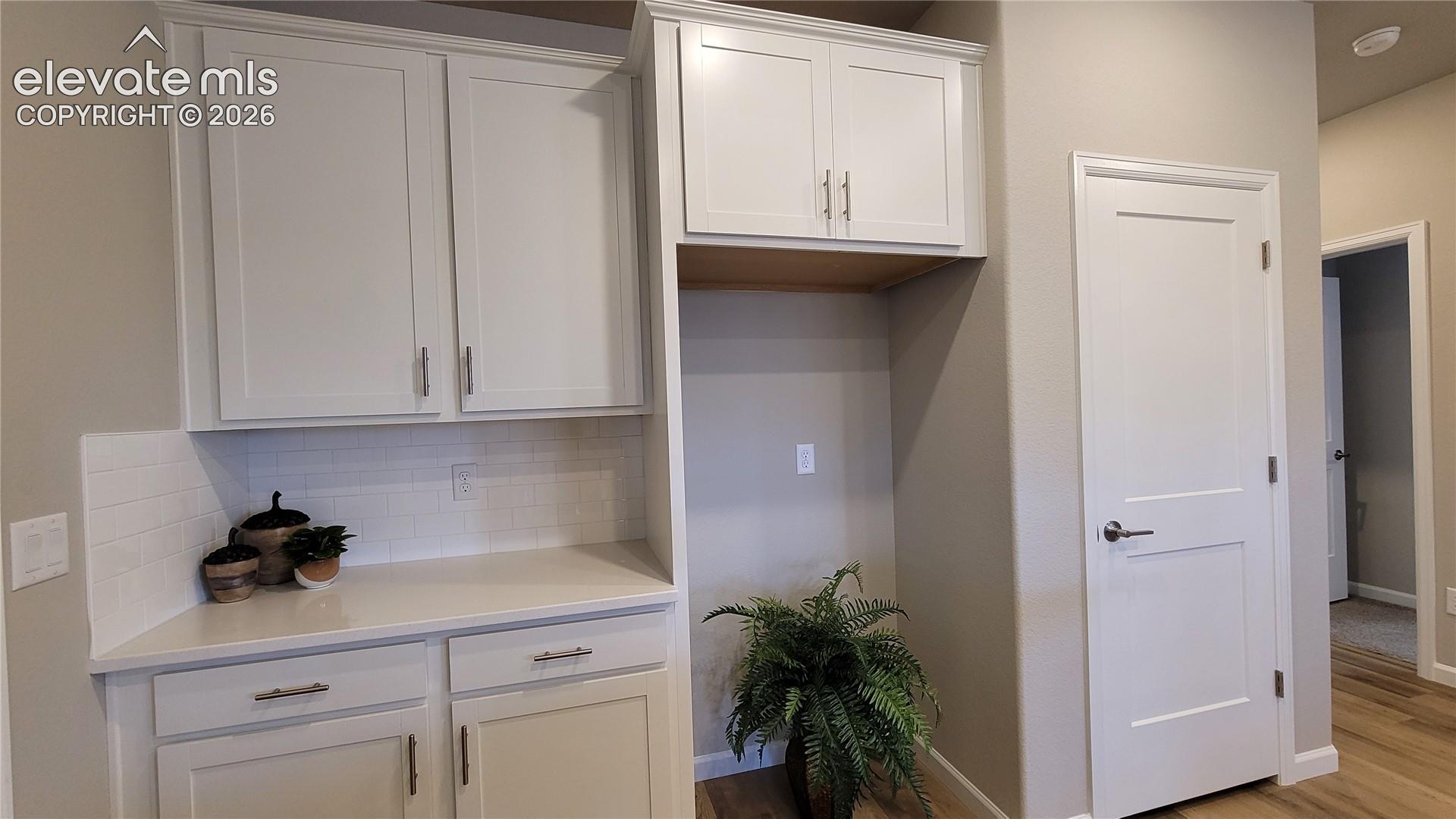 Kitchen featuring white shaker-style cabinetry, quartz countertops, a central island with a stainless steel sink, LED lighting, and LVP flooring, pantry with wood shelving, and stainless steel gas range, microwave, and dishwasher!