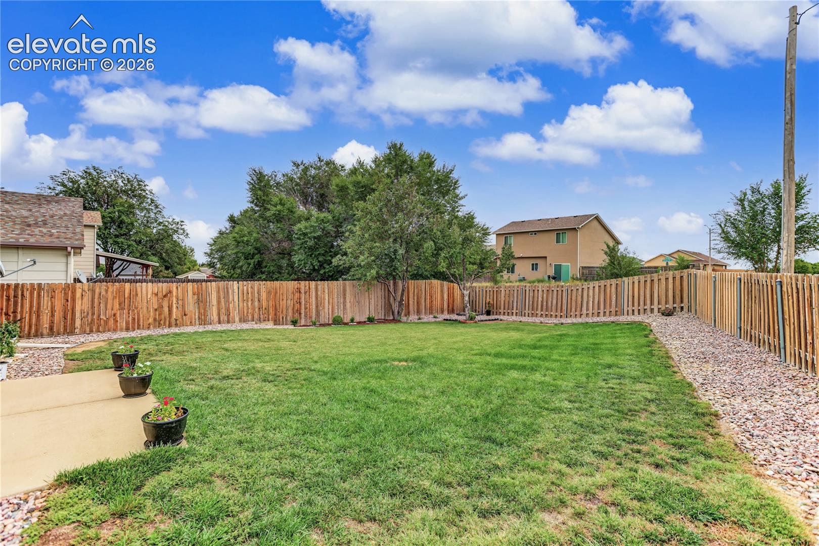 Expansive backyard featuring a manicured lawn, full privacy fencing, and a concrete patio