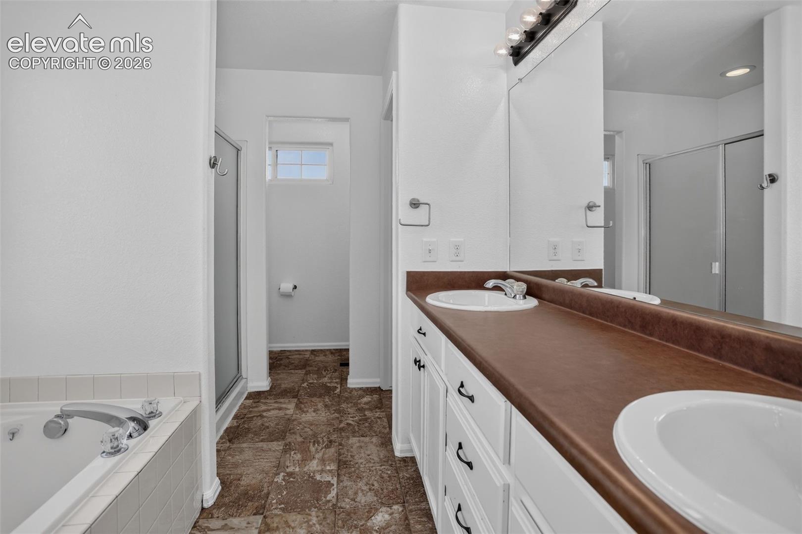Dual basin vanity with white cabinetry, integrated mirror, large soaking tub, and enclosed shower