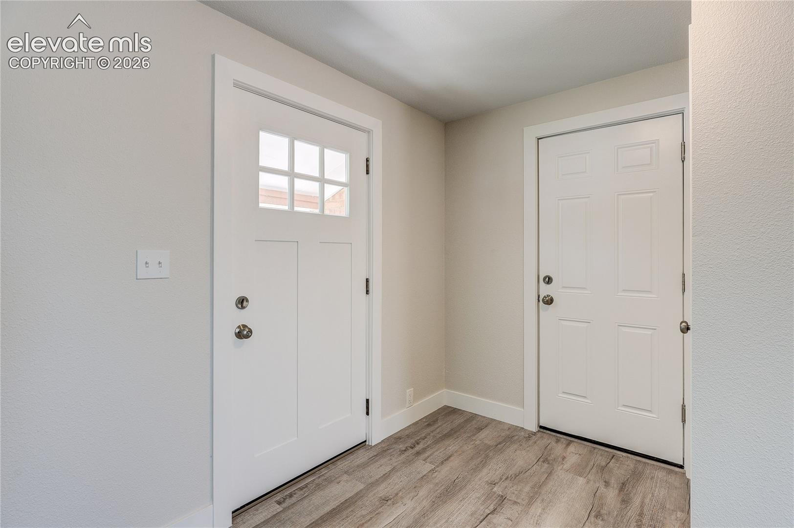 Entry area featuring wood-finish flooring, a white six-panel door, and a white craftsman-style door with a six-pane window insert