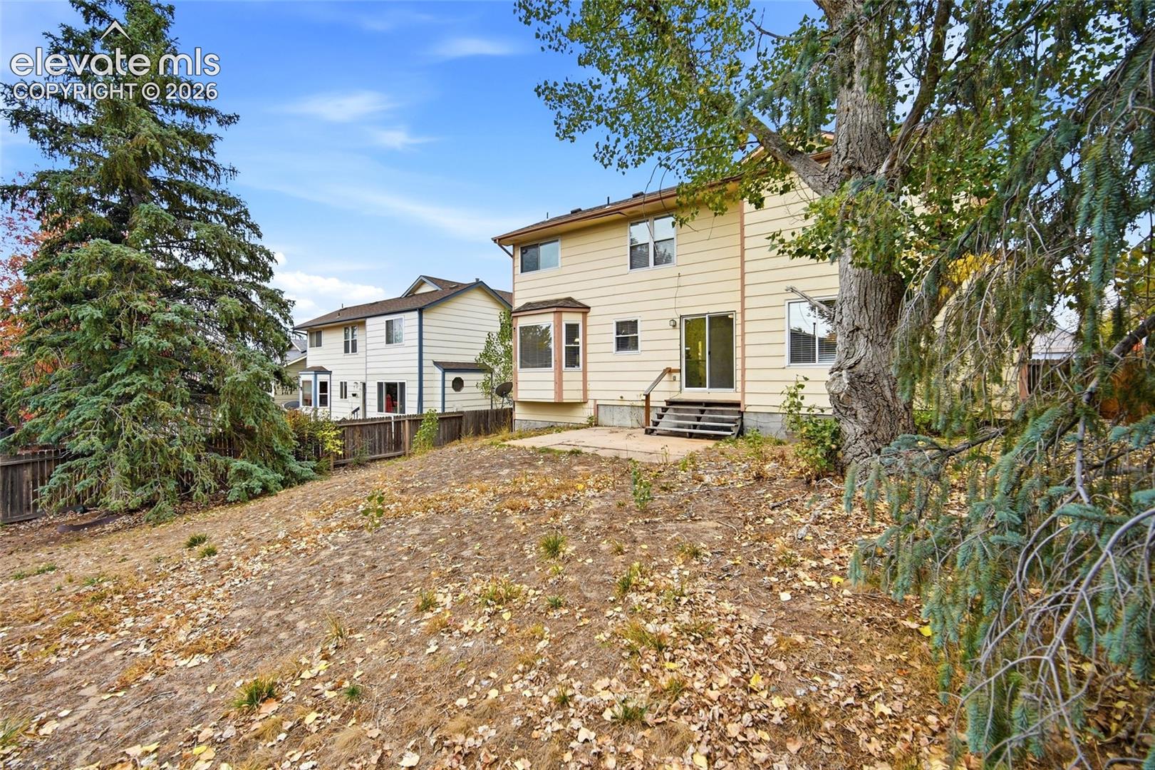 Rear exterior featuring light-colored horizontal siding, a concrete patio, a bay window, and mature evergreen trees