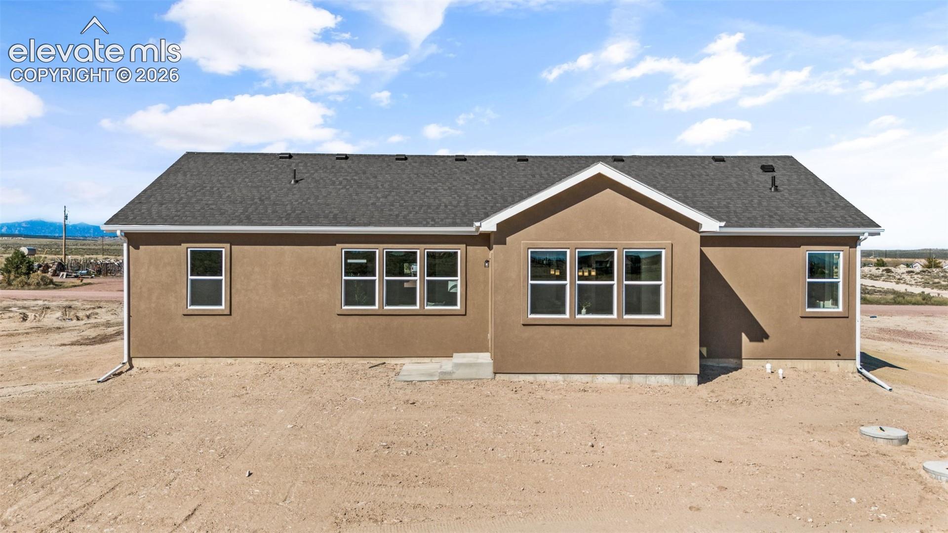 Stucco exterior with a dark shingle roof, white trim, and multiple windows