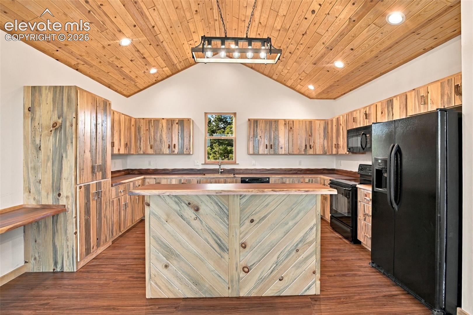 Kitchen featuring custom wood cabinetry, a central island with a live-edge countertop, vaulted wood-plank ceiling, wood-finish flooring, and a linear pendant light fixture