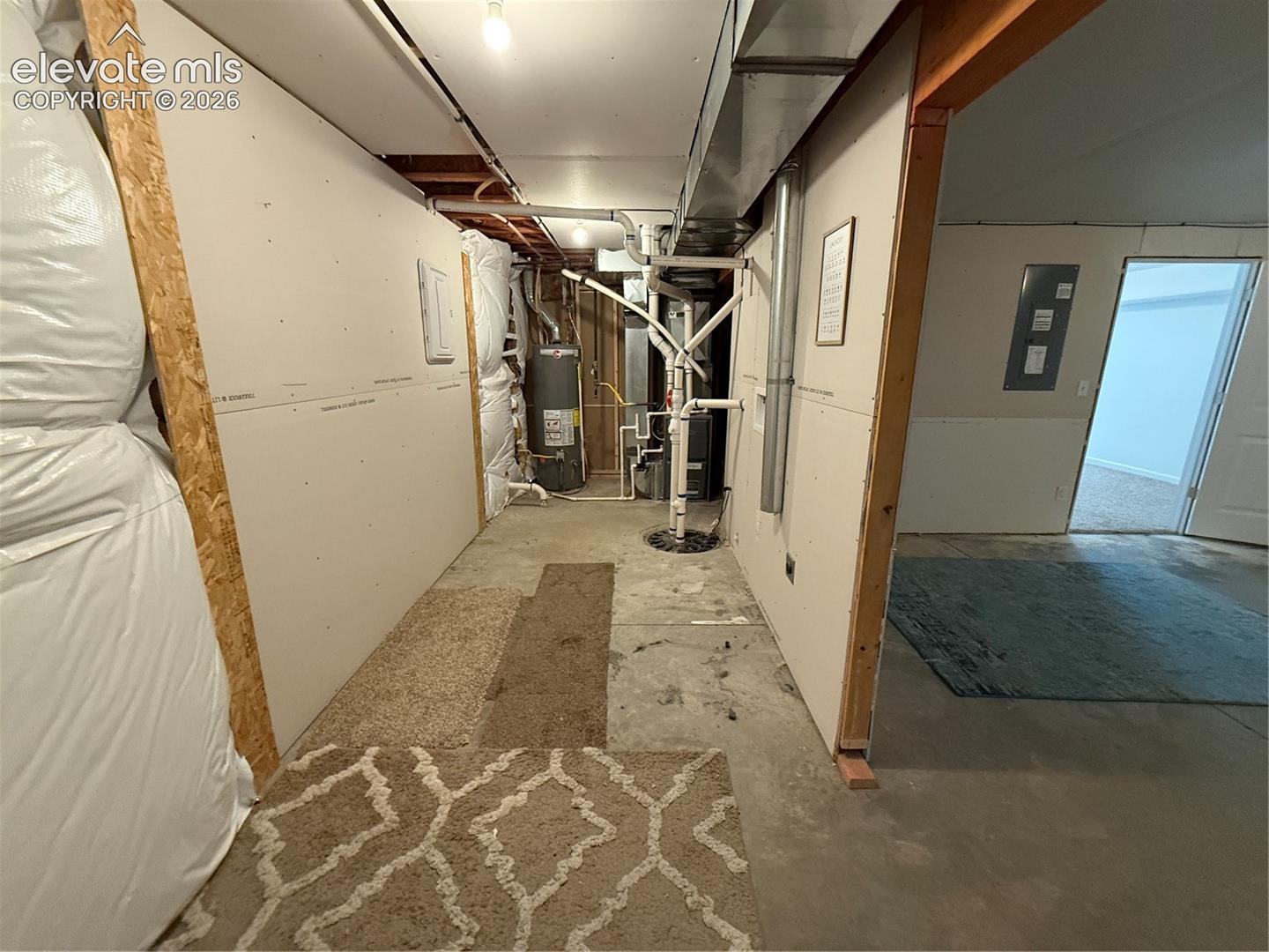 Utility area featuring concrete flooring, exposed overhead ductwork, drywall paneling, and an installed water heater