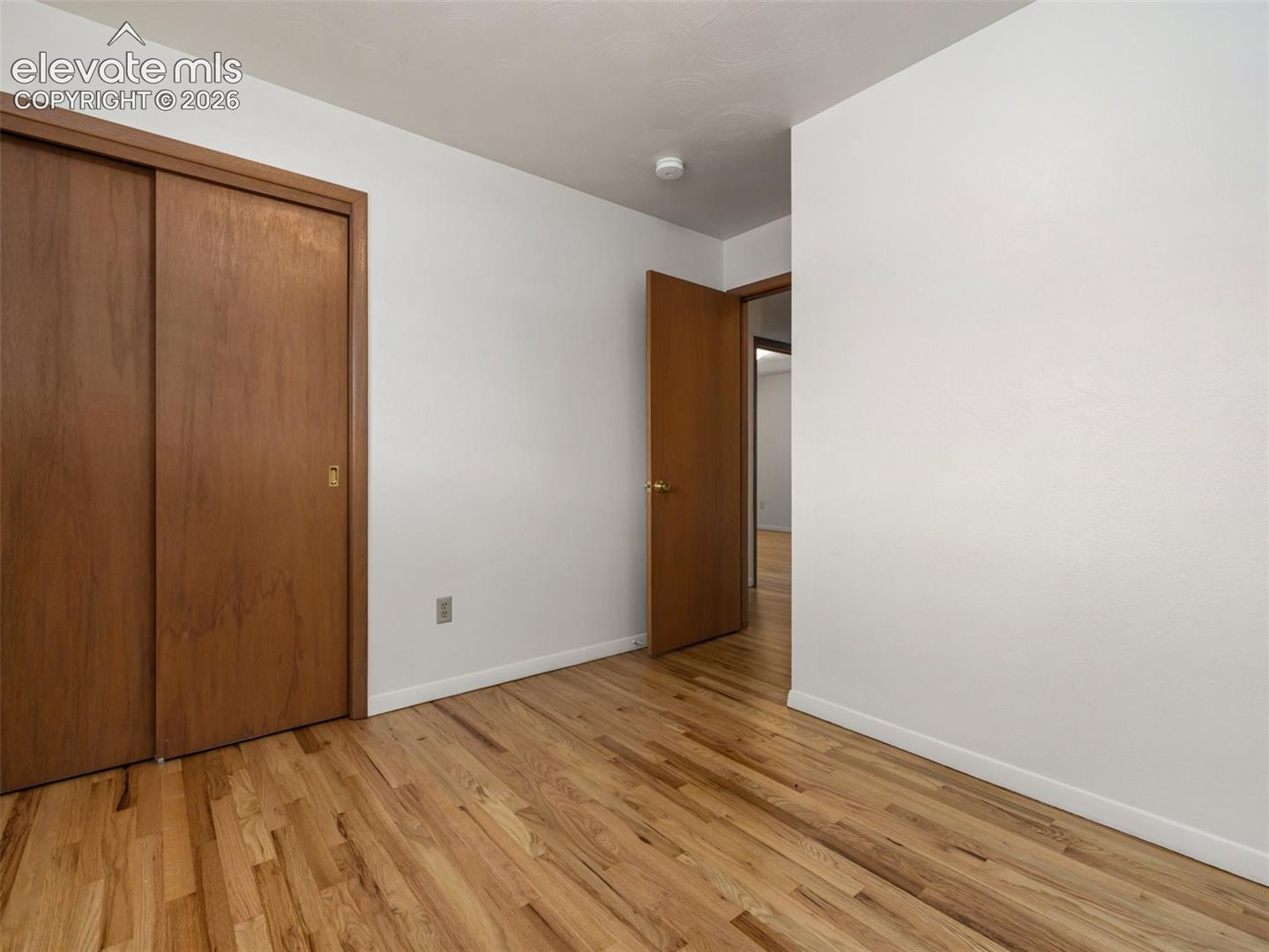 Wood-finish flooring throughout, white walls, and a sliding door closet with wood-finish doors