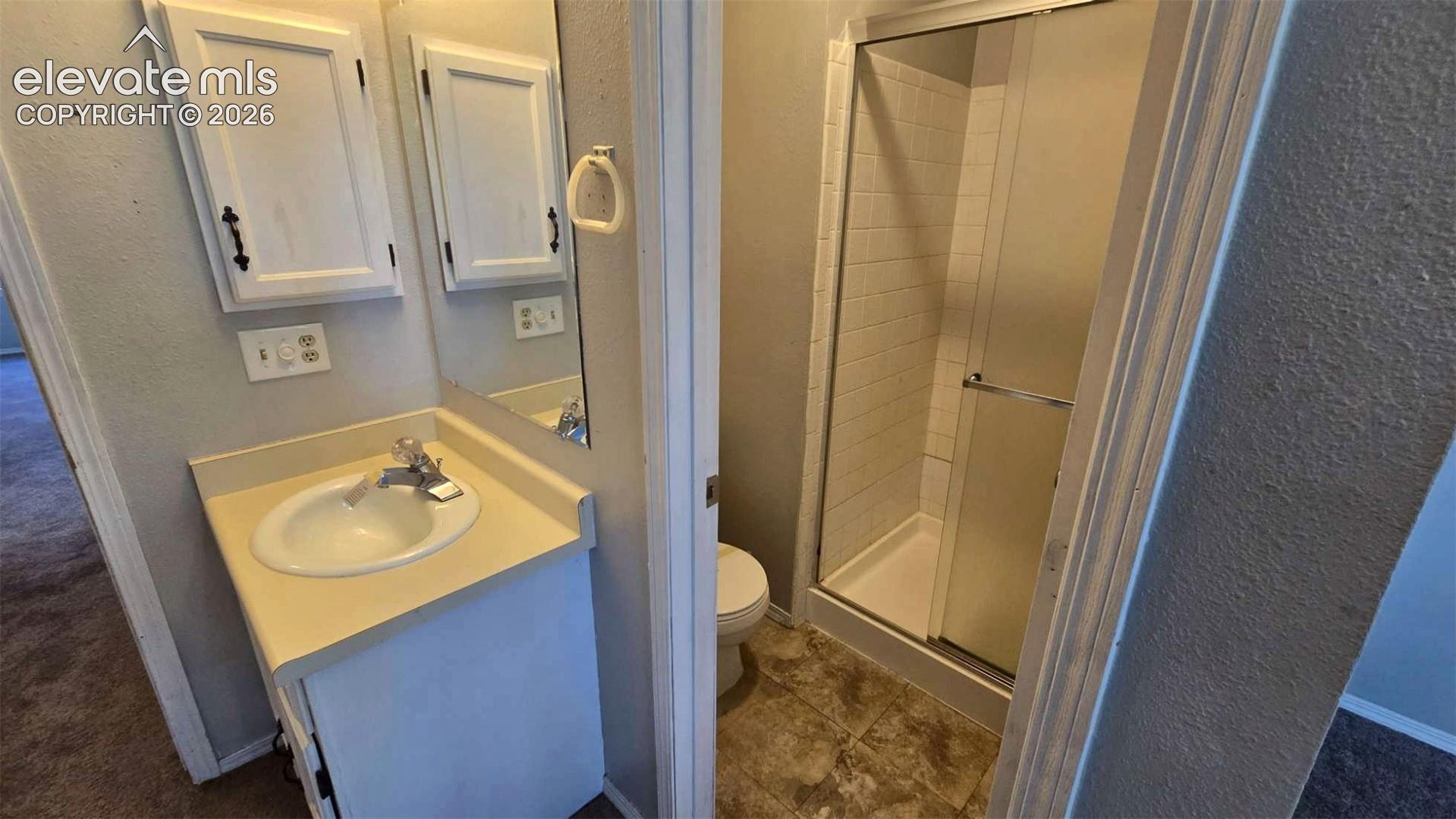 Bathroom featuring a vanity with a drop-in sink, wall-mounted cabinetry, a tiled shower enclosure with a glass door, and tile flooring