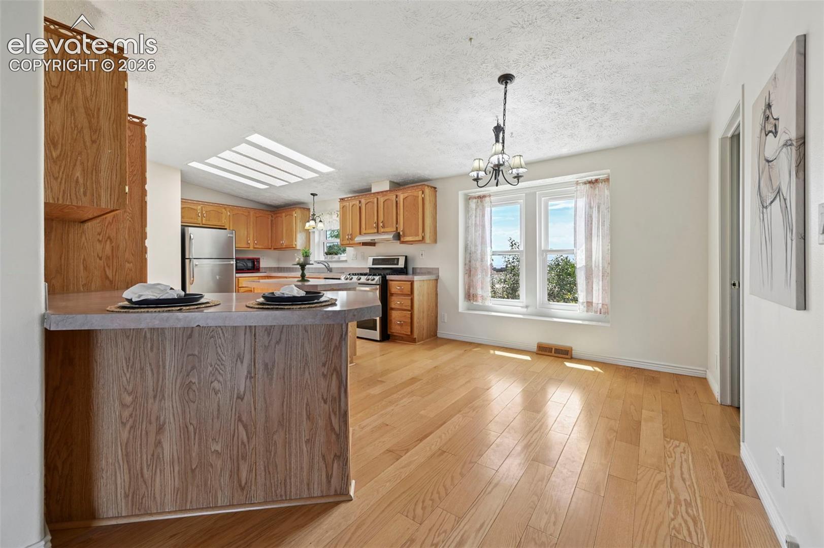 Kitchen featuring wood cabinetry, stainless steel appliances, a skylight, and a breakfast bar