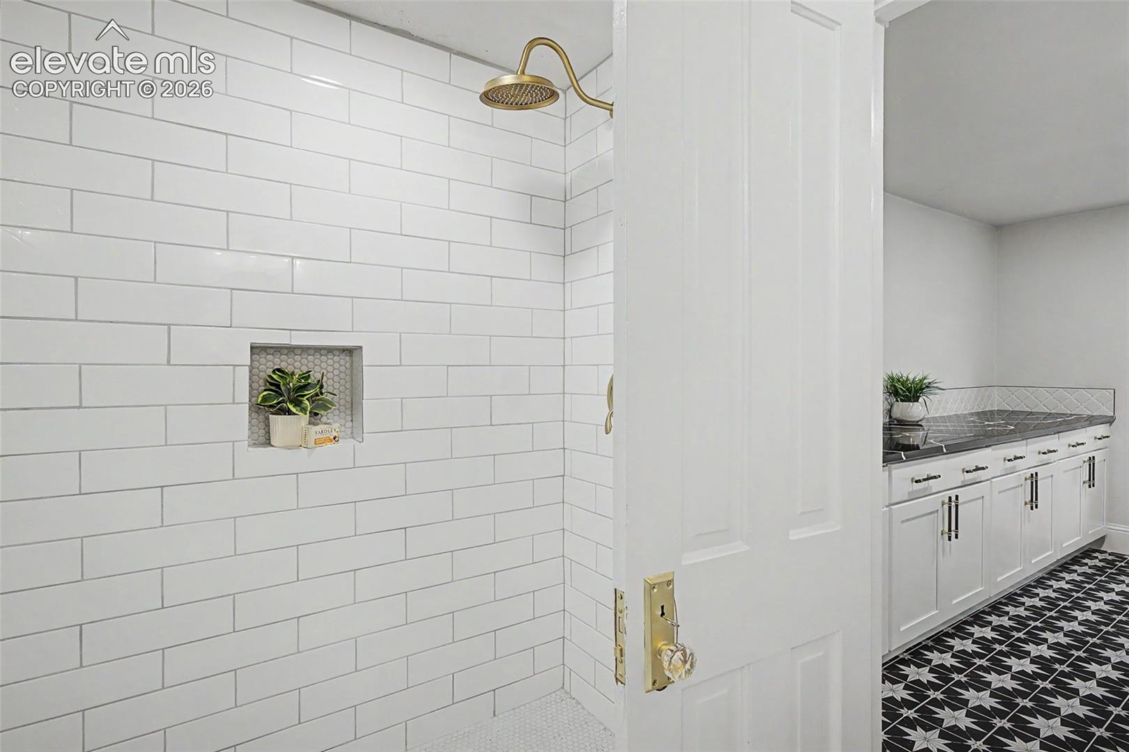 Shower enclosure with white subway tile walls, a built-in niche with hexagonal mosaic tile, and a gold-finish shower head