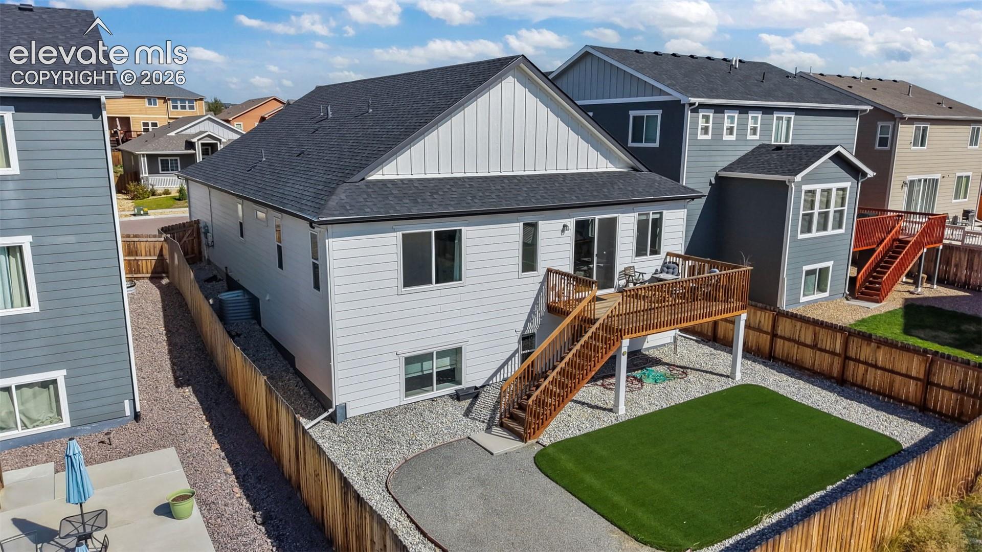 Upper-level wood deck with staircase, sliding glass door access, fenced perimeter, gravel landscaping, and artificial turf area