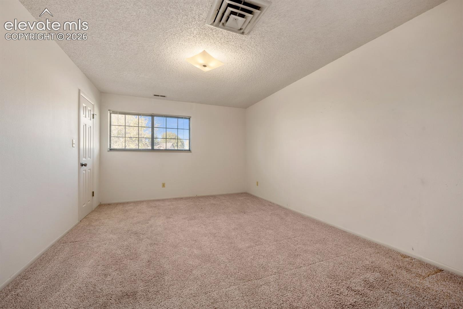 Room featuring neutral carpeting, a single-panel interior door, a horizontal sliding window, and a ceiling-mounted light fixture