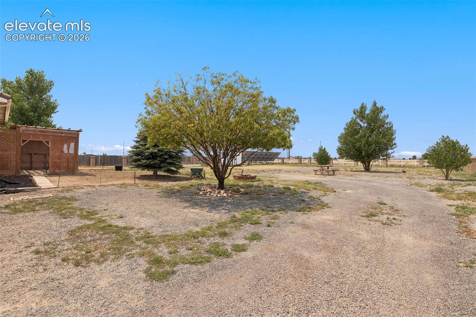 Expansive grounds featuring a gravel surface, mature trees, a detached masonry structure, and solar panel array