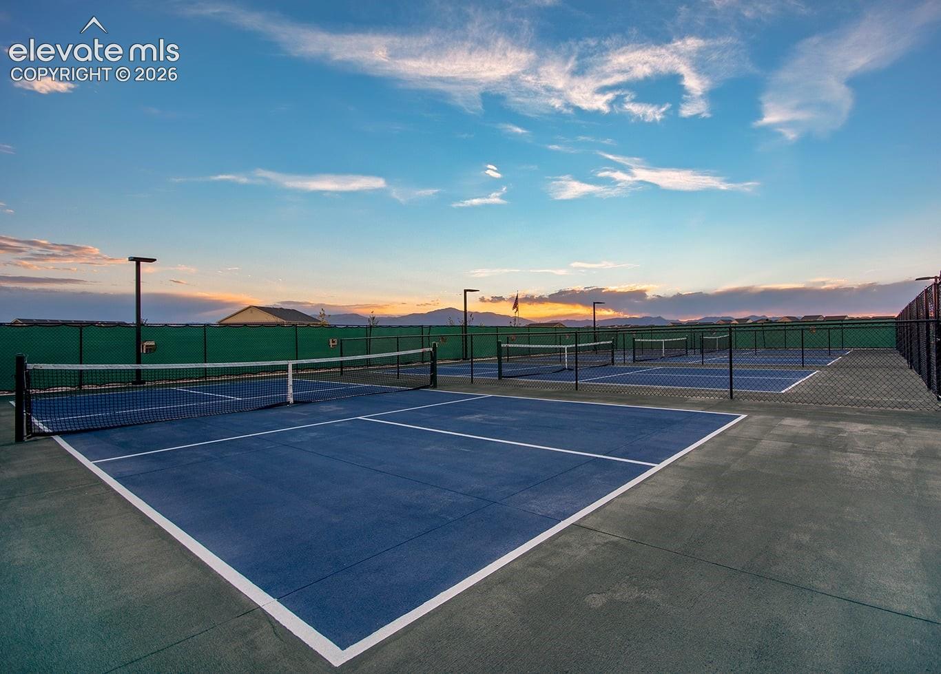Multi-court recreational facility featuring hard-surface playing areas, perimeter chain-link fencing with privacy screens, and integrated court lighting