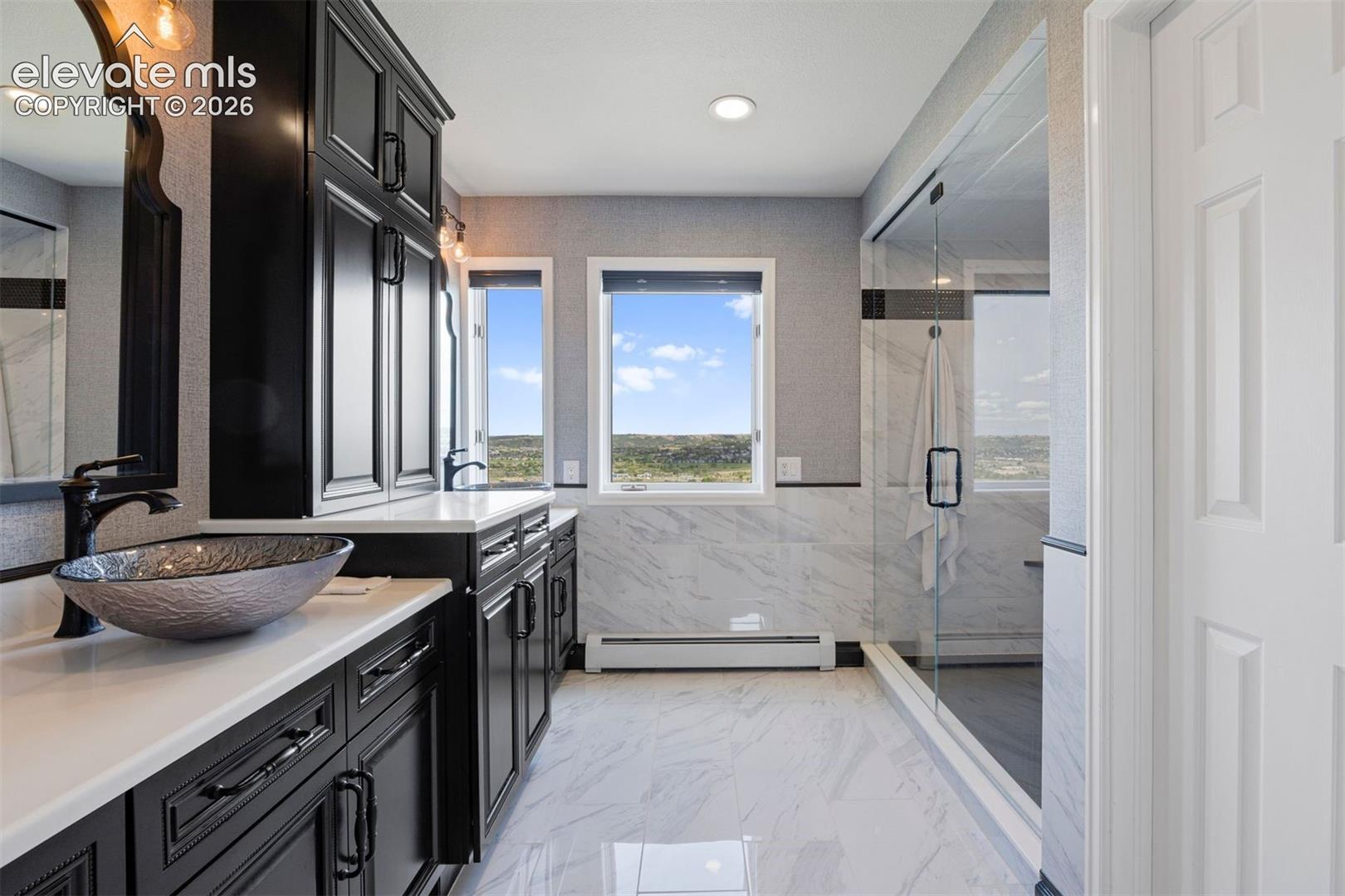 Primary bath with dual vessel sinks, dramatic black cabinetry, quartz counters, and marble shower. 