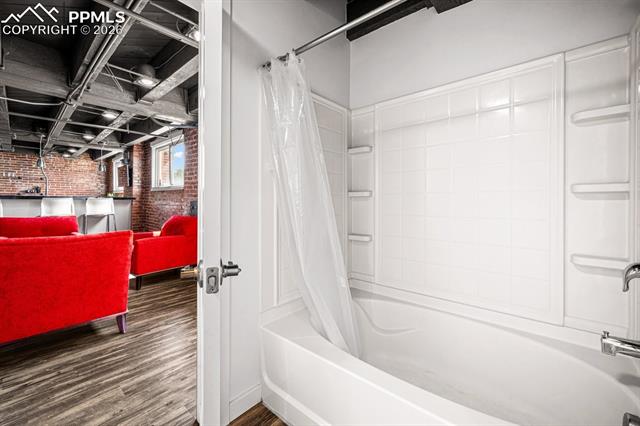 Full bath with brick wall, shower / bath combo with shower curtain, and wood finished floors