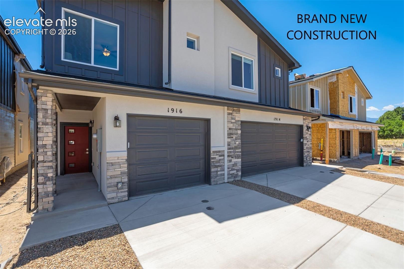 Modern multi-family exterior featuring mixed-material siding, stacked stone accents, dual-car garages, and a concrete driveway