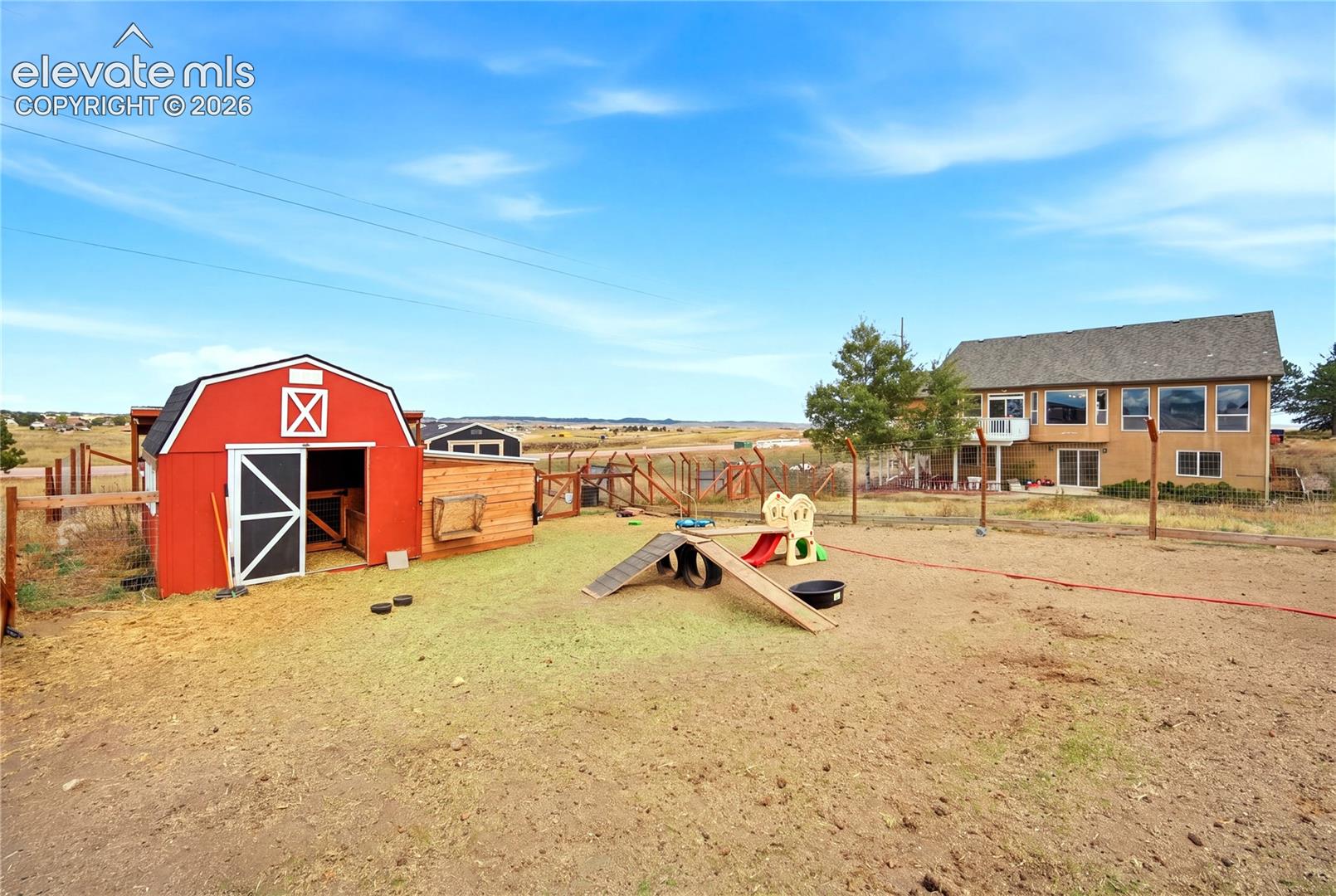 Expansive outdoor area featuring a red barn-style structure with metal roof, perimeter wood fencing, and multi-level residence with large windows