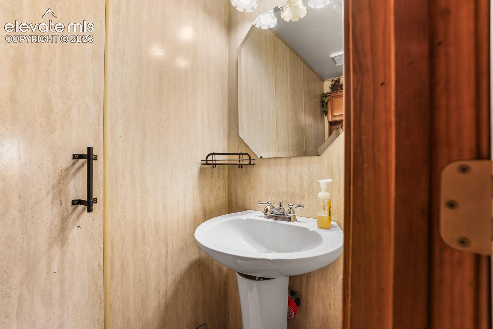 Pedestal sink with chrome faucet, octagonal mirror, and wall-mounted light fixture