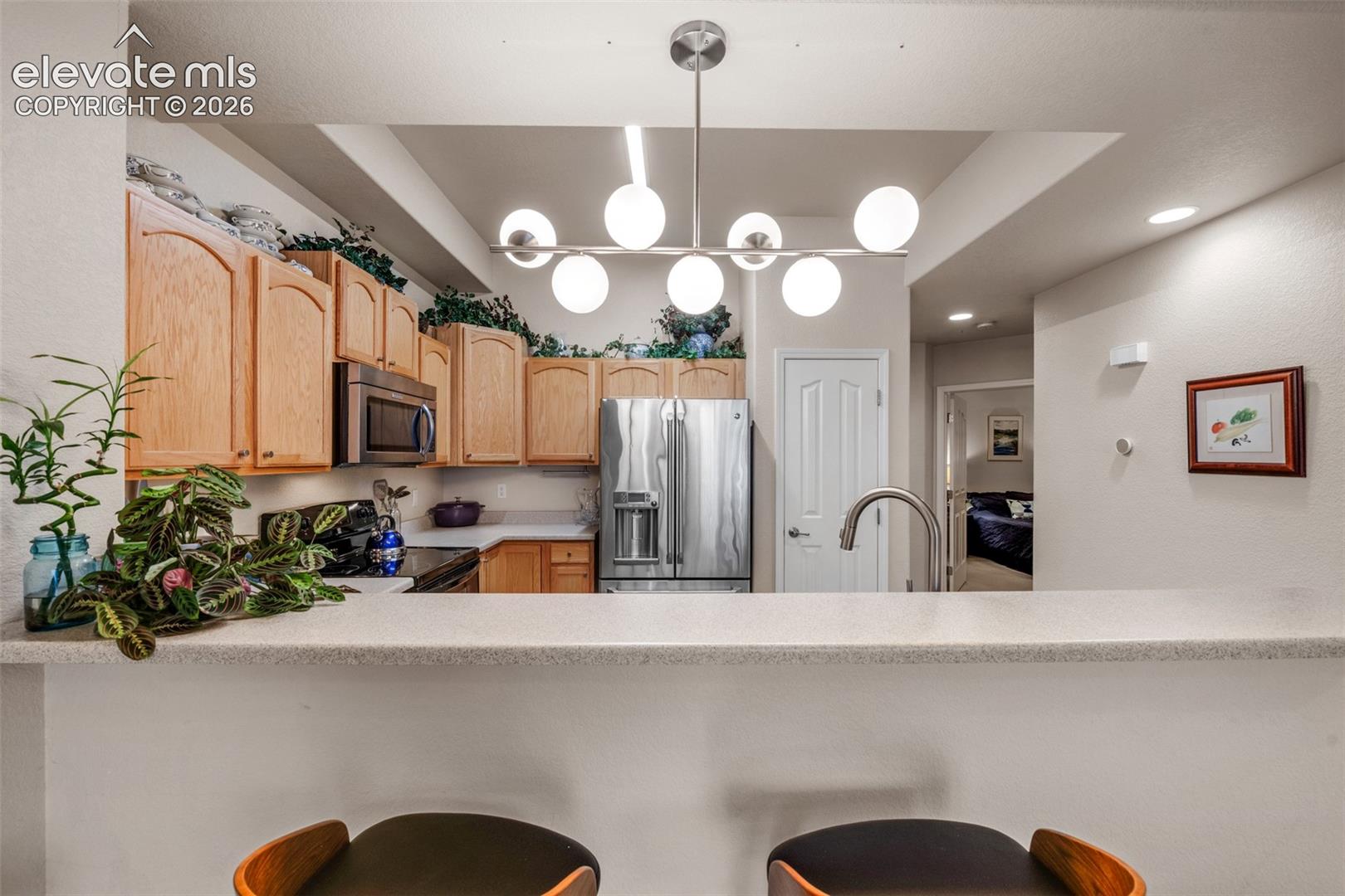 Kitchen featuring wood cabinetry, stainless steel appliances, a bar-height counter, and a contemporary linear chandelier